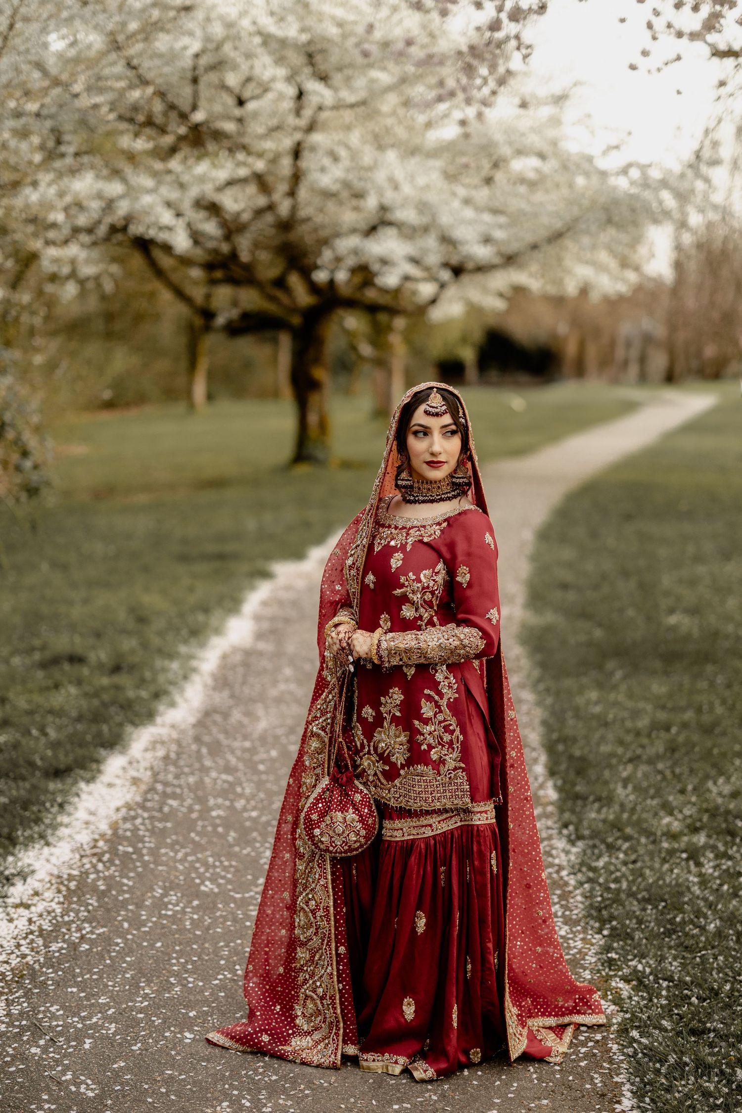 Bride in red bridal lehenga walking garden path, Muslim wedding photoshoot