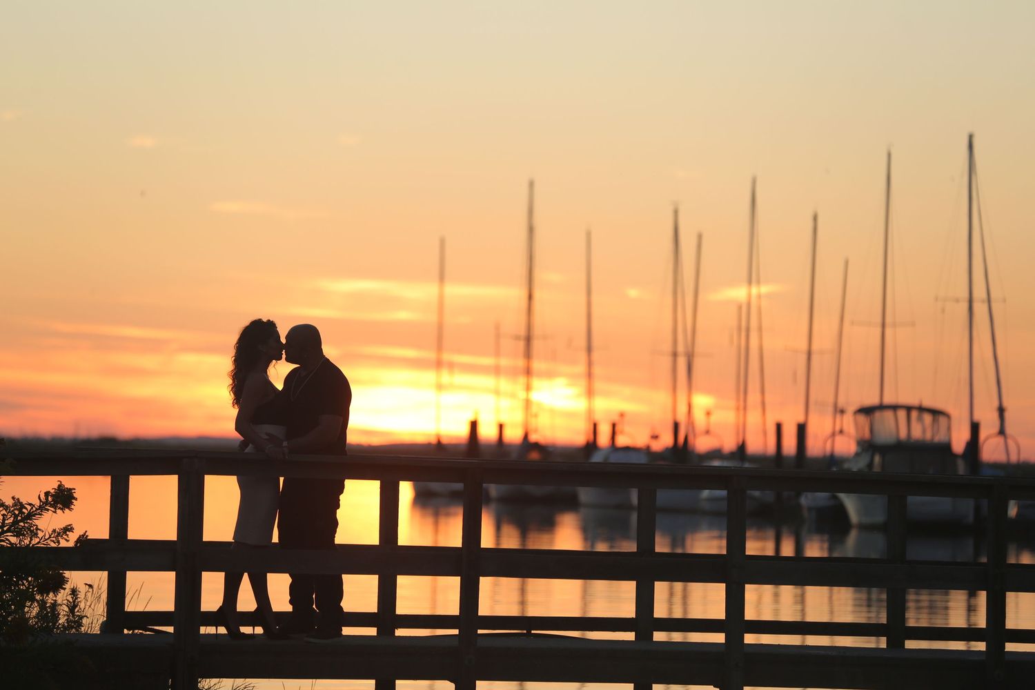Silhouette of couple embracing at sunset by marina, golden hour engagement photos