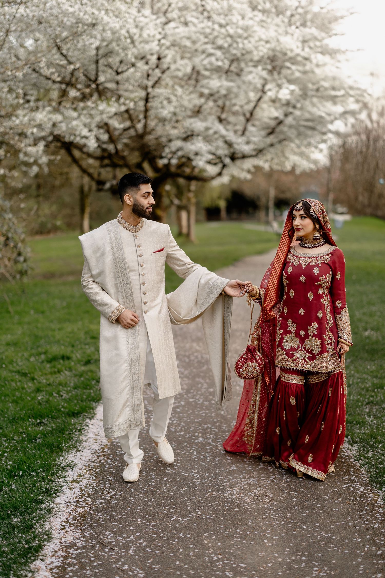 Muslim Bride and groom walking together, red bridal lehenga, spring blossom setting