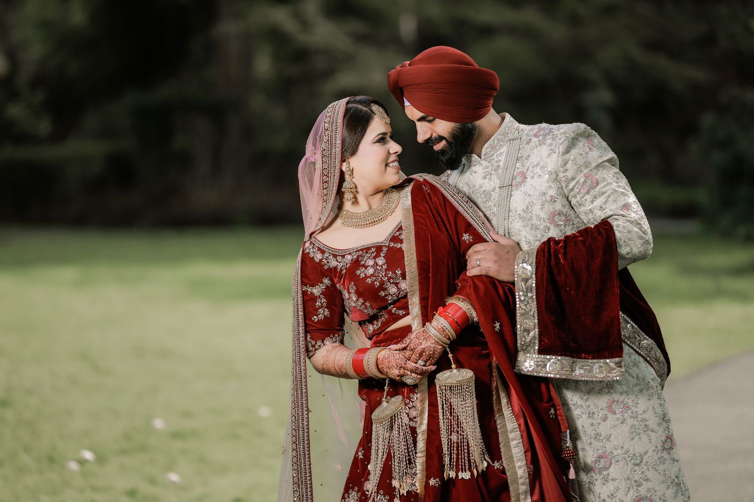 Punjabi bride and groom in red and gold wedding attire, outdoor portrait