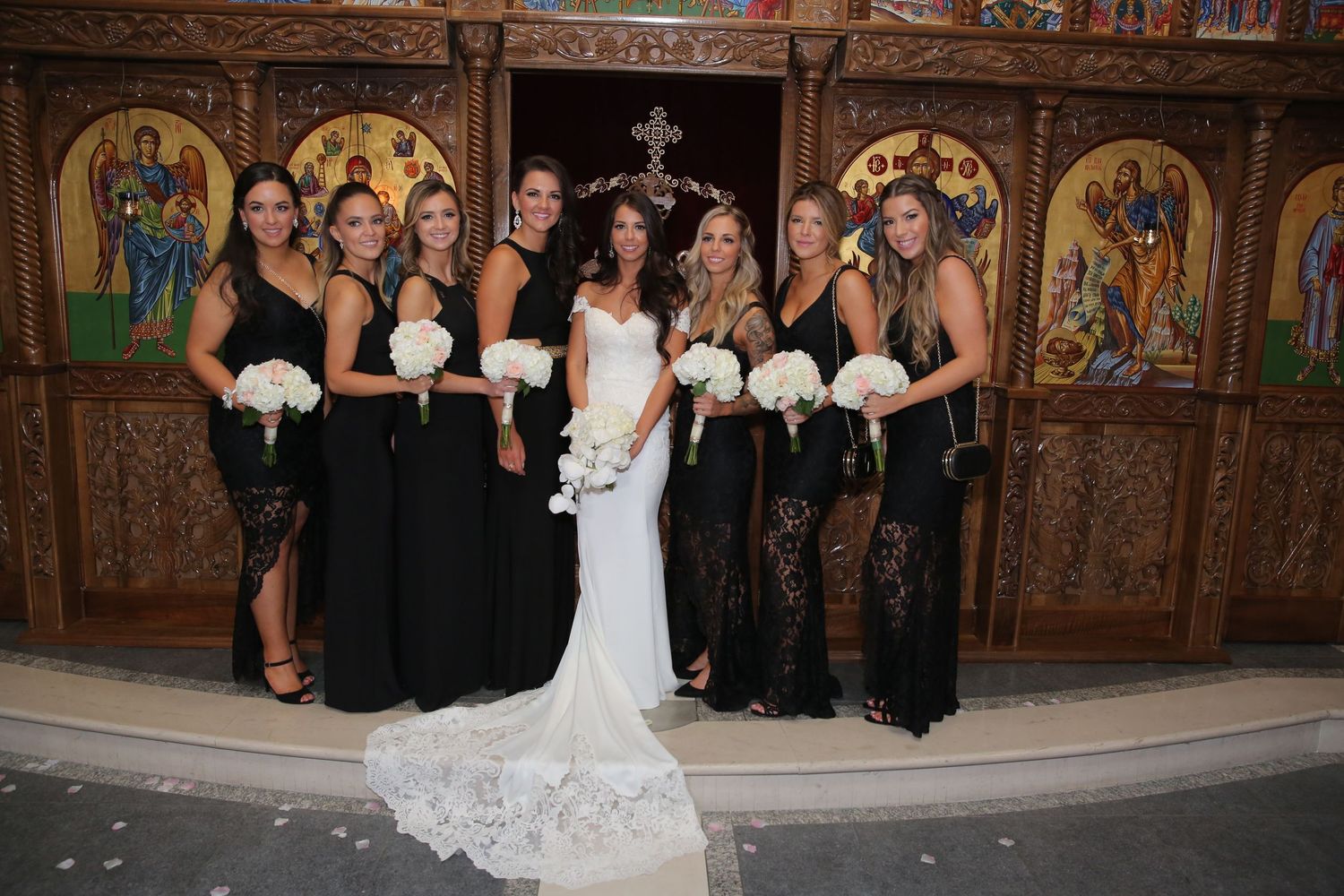 Bride with bridesmaids in black gowns in front of ornate church, Vancouver wedding photography