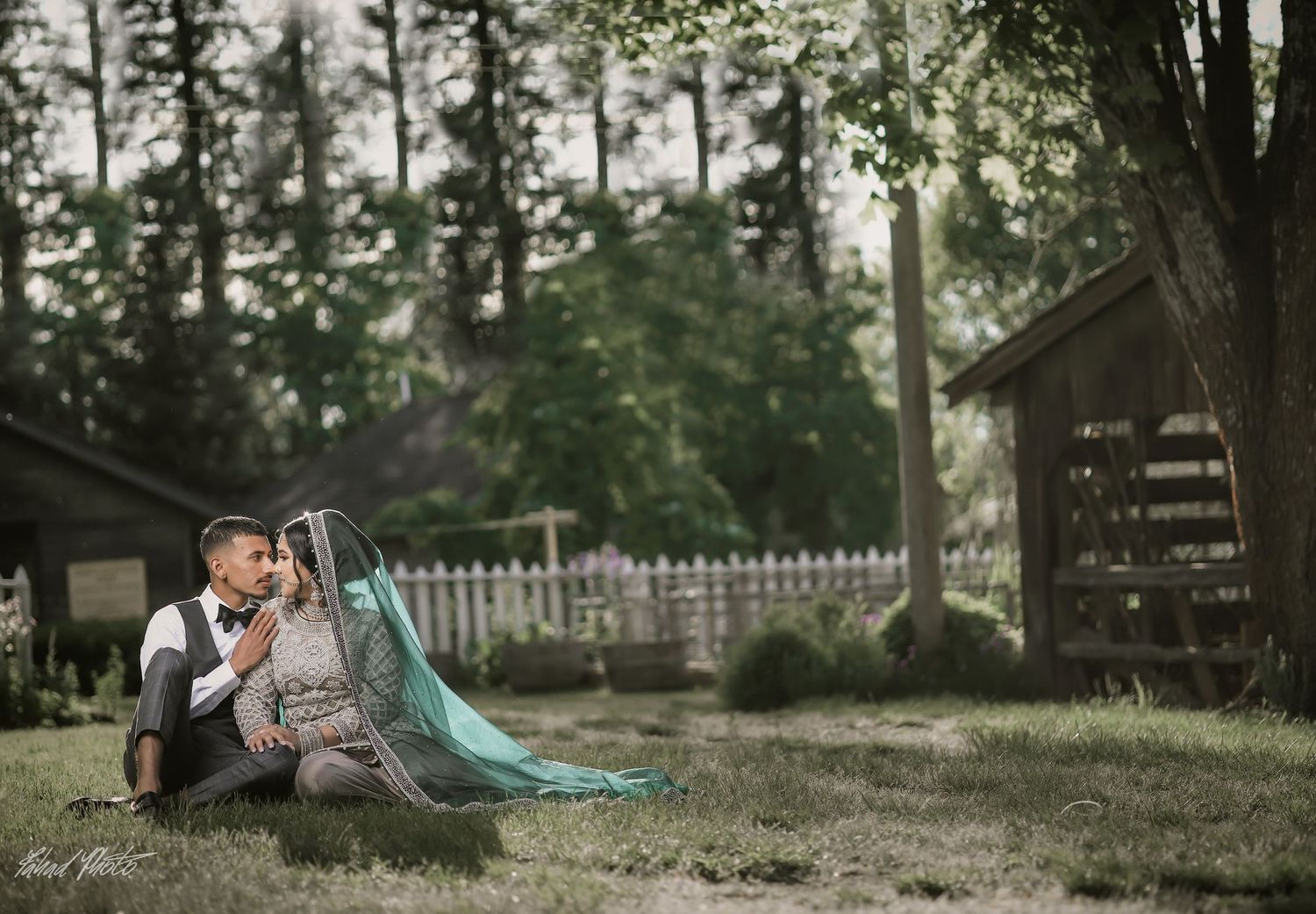 Couple seated outdoors in rustic setting, teal dupatta flowing, engagement shoot