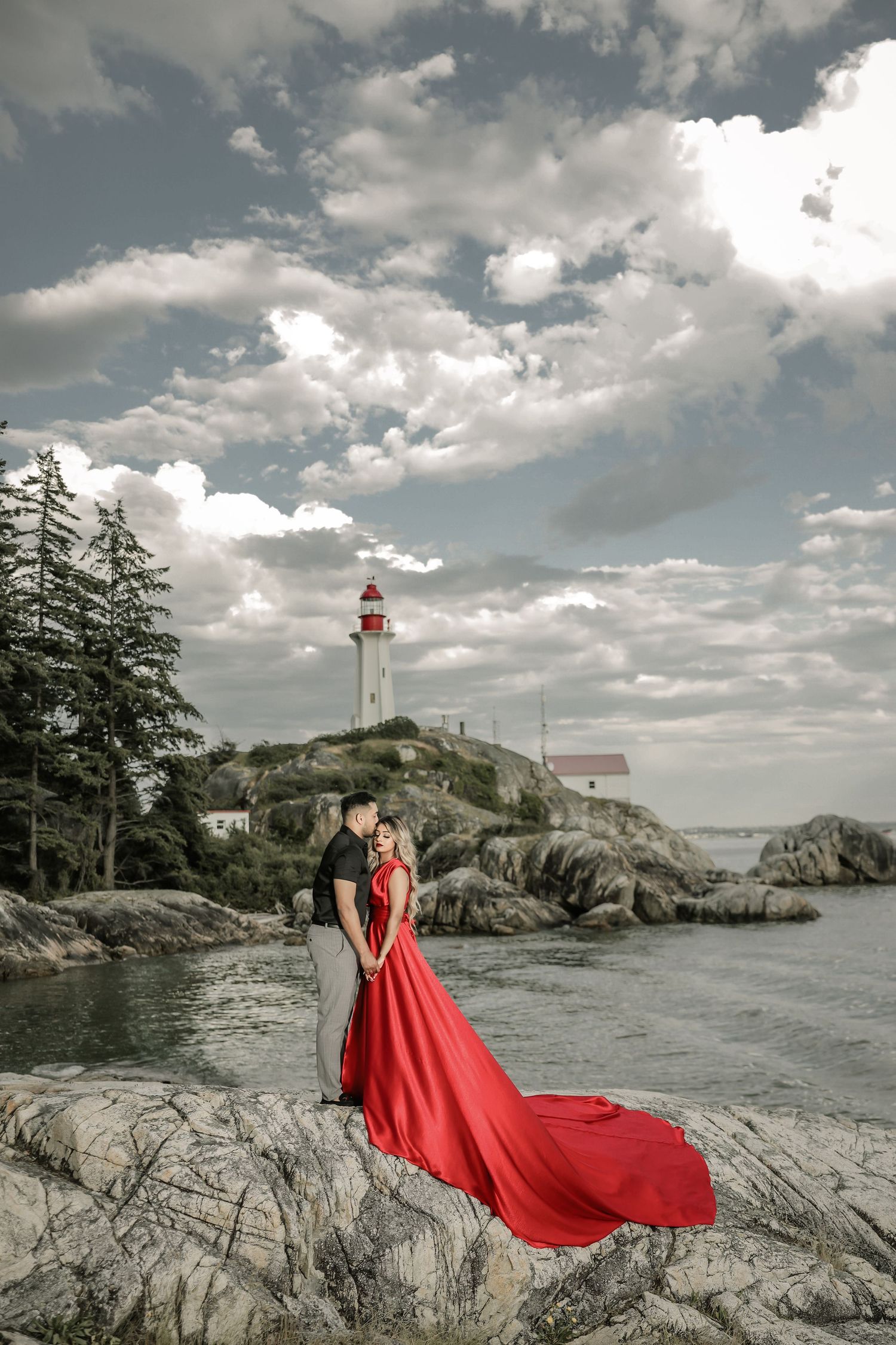 Bride in flowing red gown on coastal rocks near lighthouse, BC pre-wedding shoot
