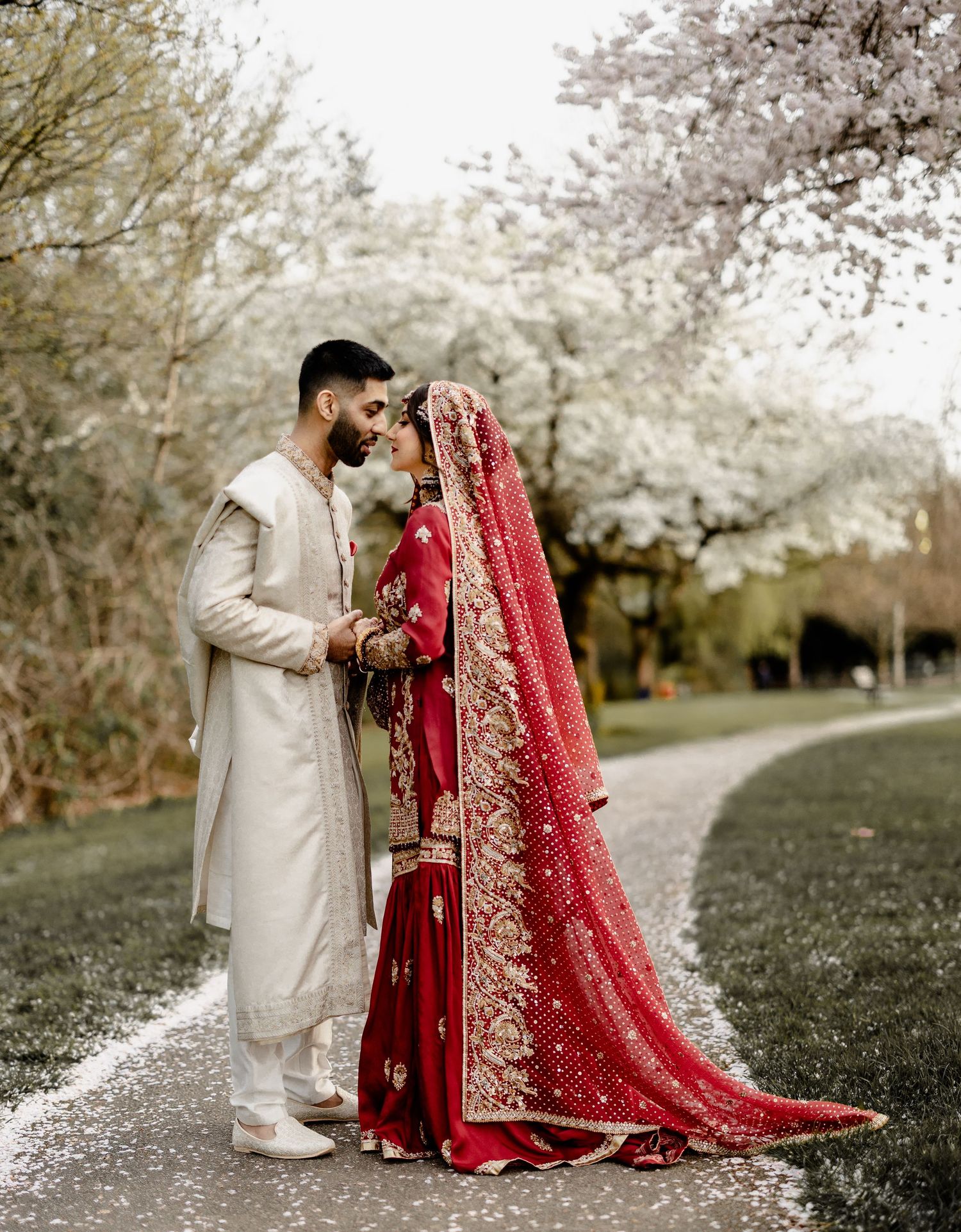 Muslim Bride and groom in coordinated red and cream attire, spring blossom backdrop