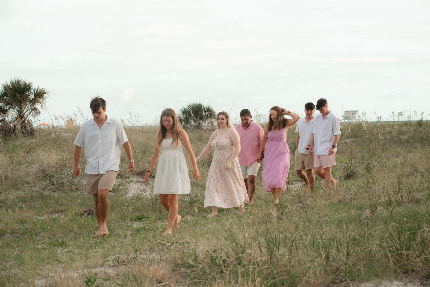 Large family portrait session with teens walking through dunes on a florida beach.