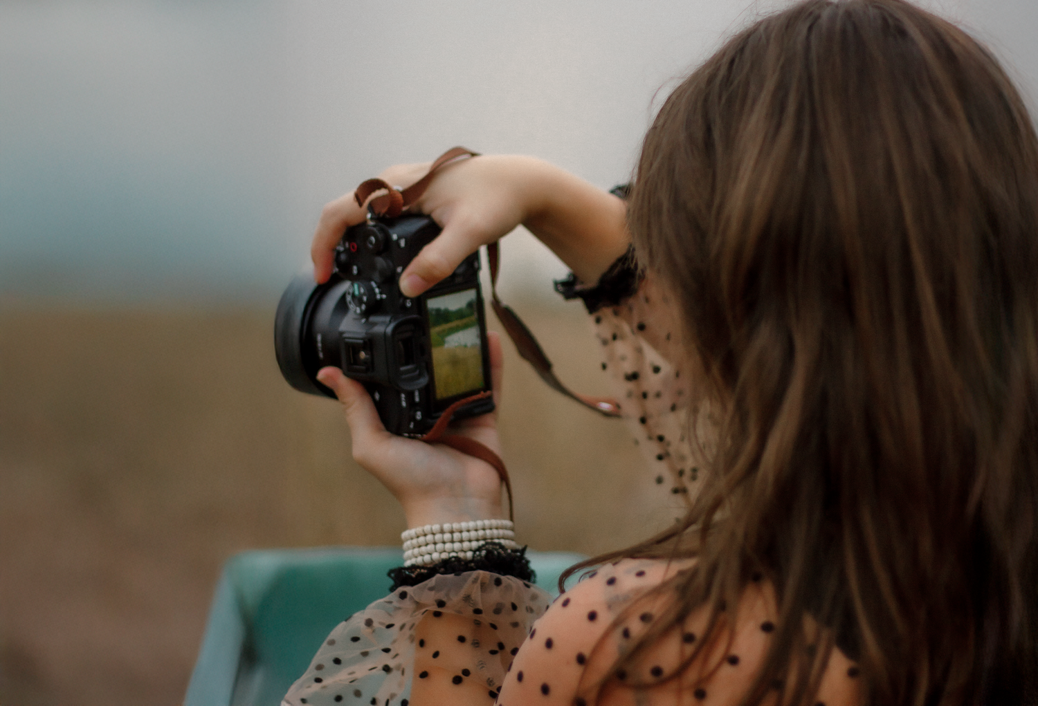 A photographer with a vintage camera in a polka dot dress lying on a teal couch in a field.