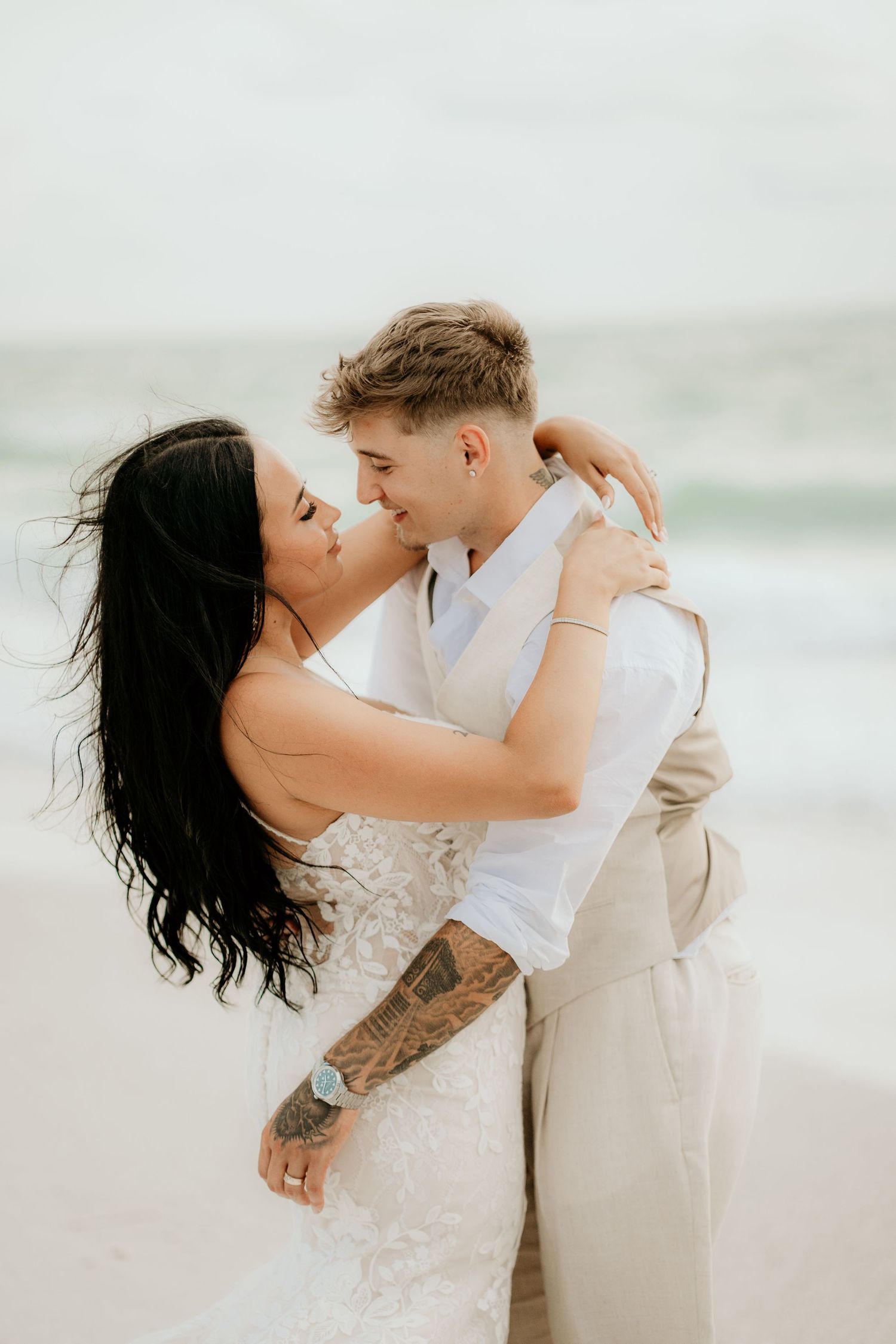 A couple embraces on a misty beach with waves and overcast sky in the background.