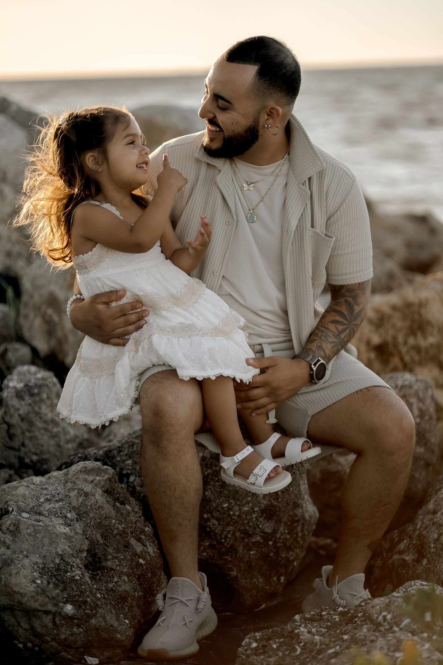 Father and daughter share joyful moments together on rocky beach at sunset.
