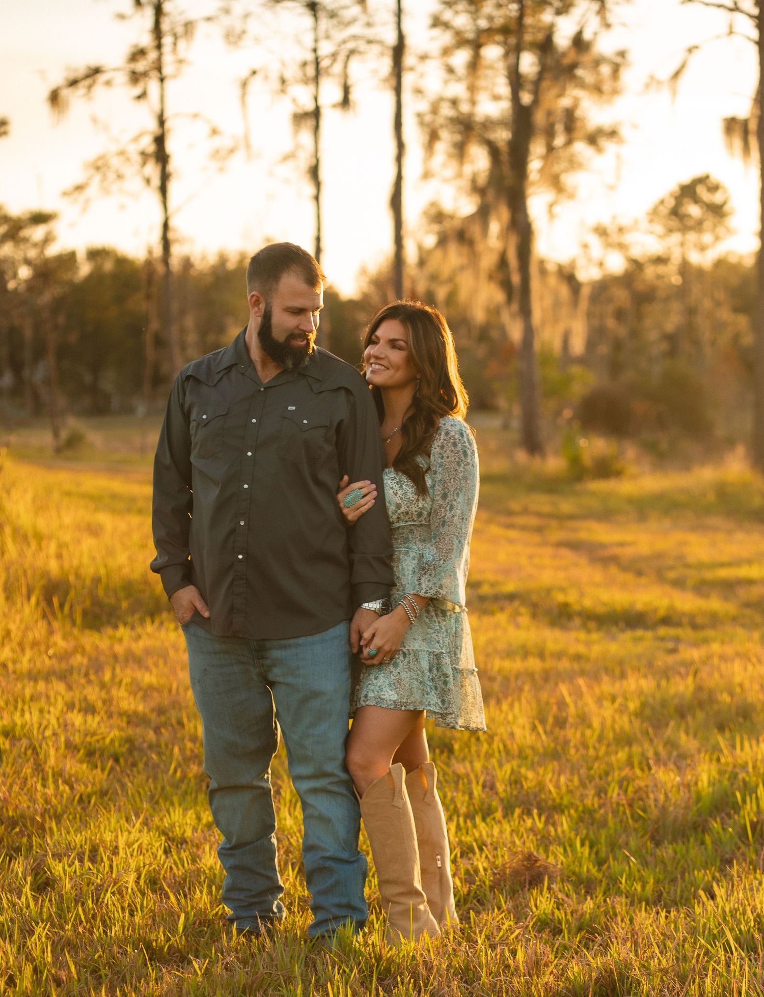 A couple shares a tender moment in a golden field at sunset, creating a romantic silhouette against the warm light.