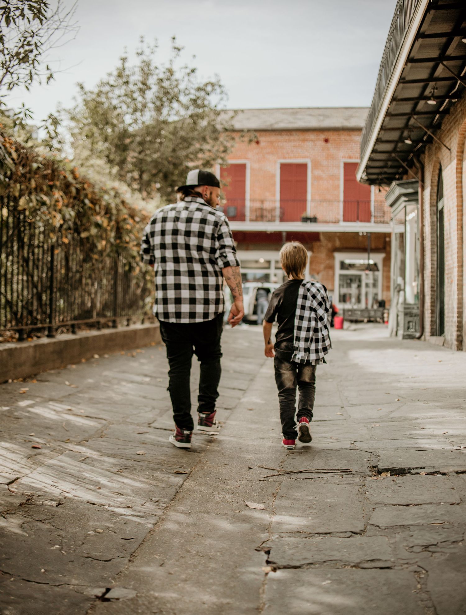Parent and child wearing matching plaid shirts walking together down a historic street.