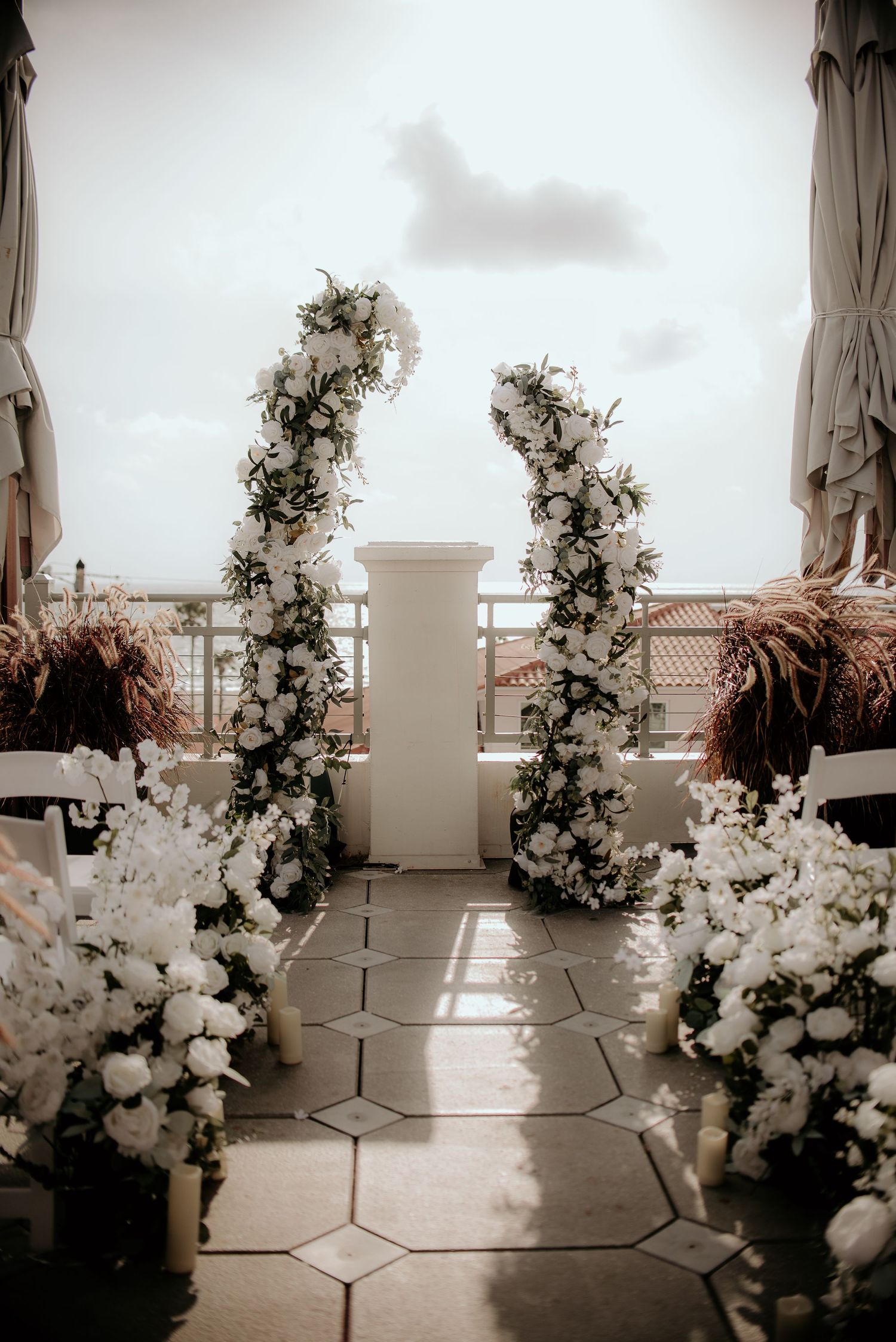 White floral wedding ceremony setup with elegant archways and pampas grass decorations.
