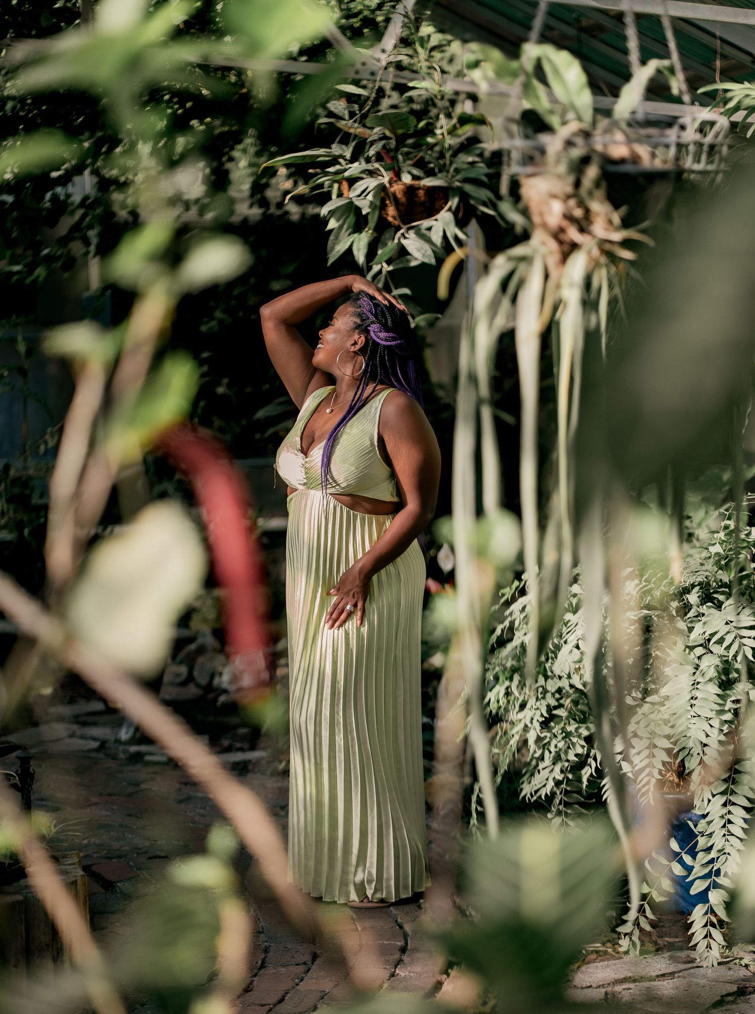 A garden photoshoot featuring someone in a flowing yellow pleated dress among leafy foliage.