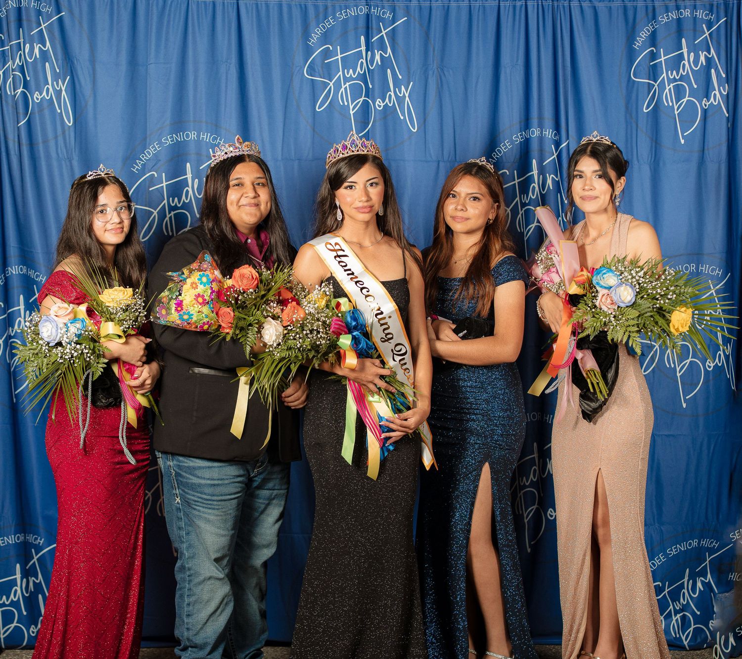 Group photo of pageant contestants holding bouquets against a blue curtain backdrop.