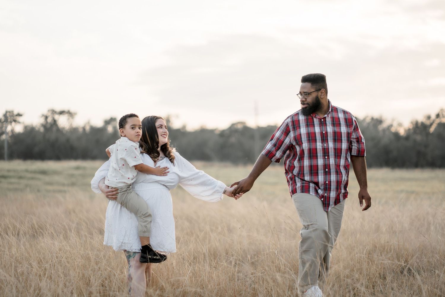 Family plays and runs together in a serene field during sunset.