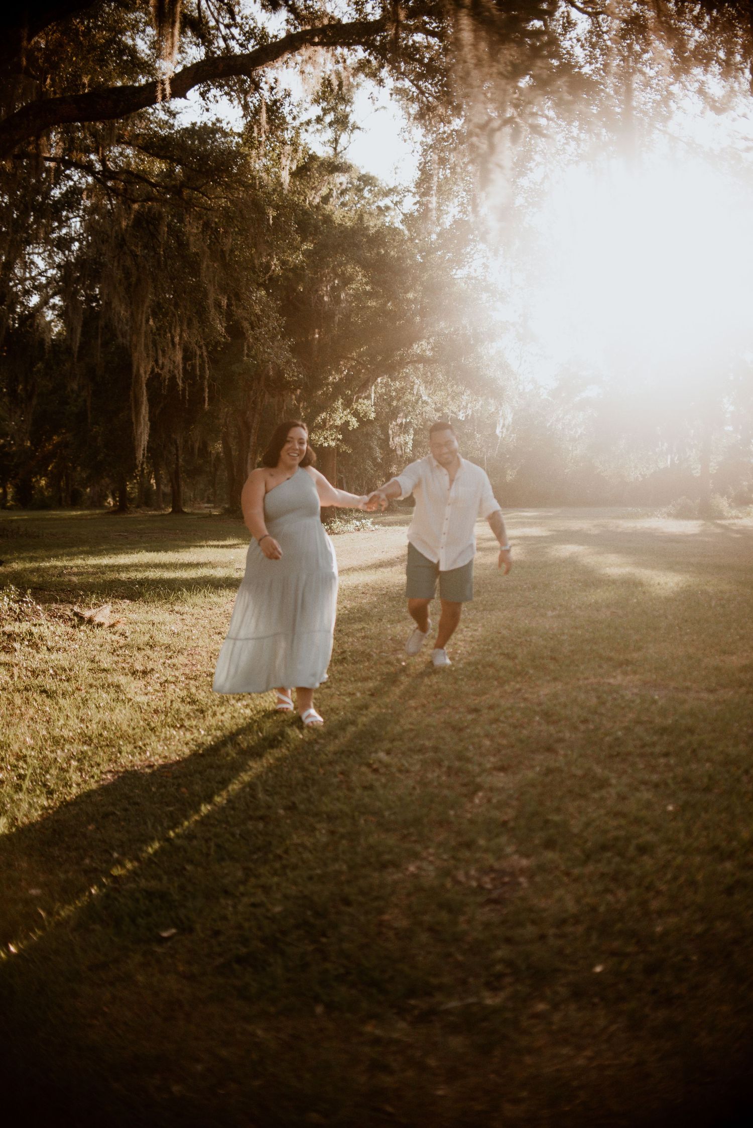 A couple runs playfully through a sunlit park during golden hour.