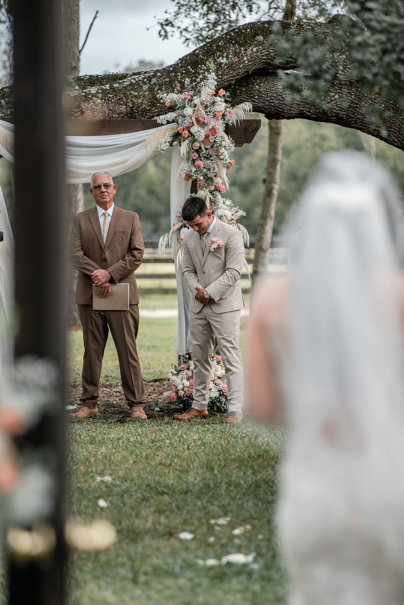 An intimate outdoor ceremony setup with floral arch and draped fabric in a garden setting.
