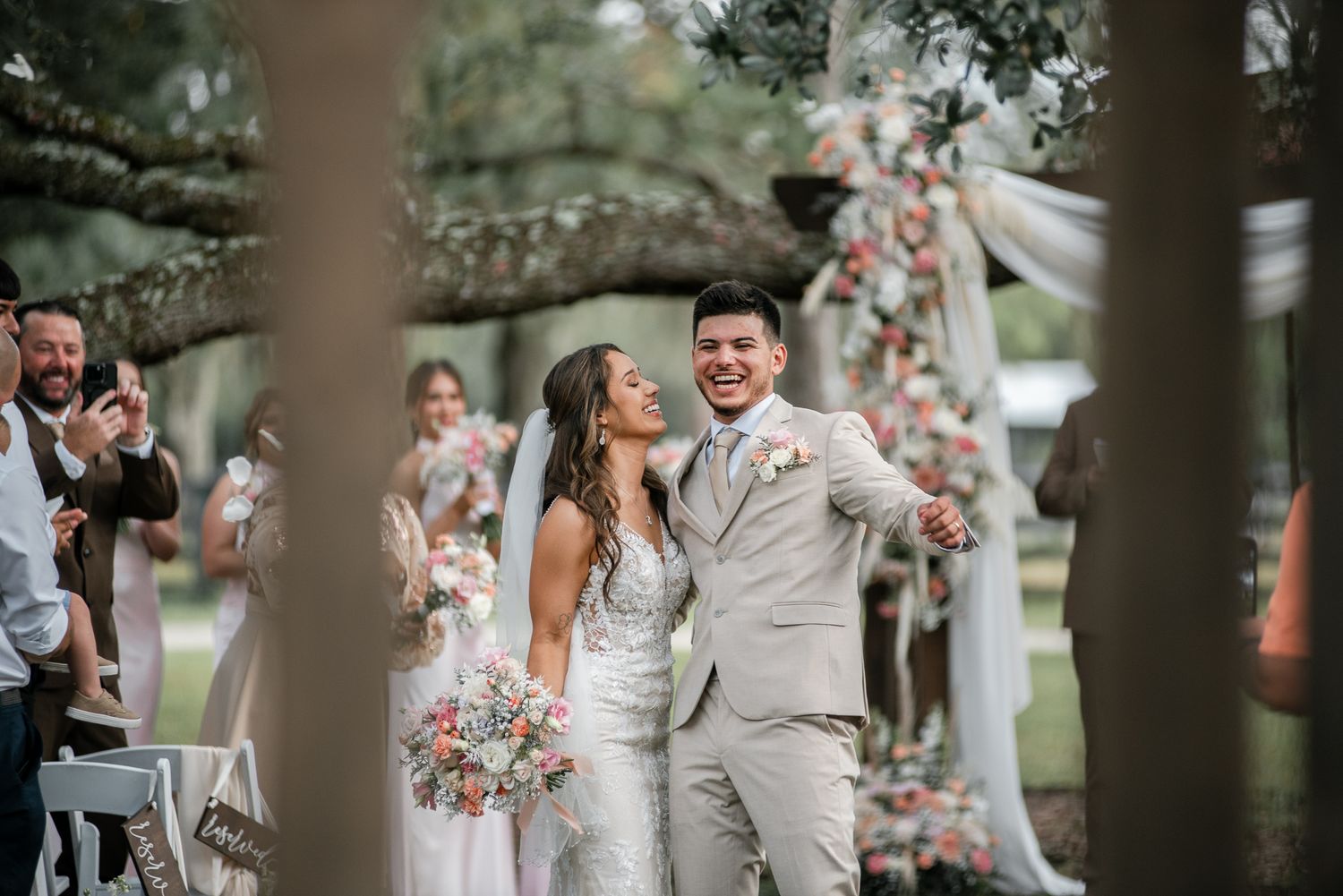 Newlyweds celebrate joyfully during their outdoor wedding ceremony under floral decorations.