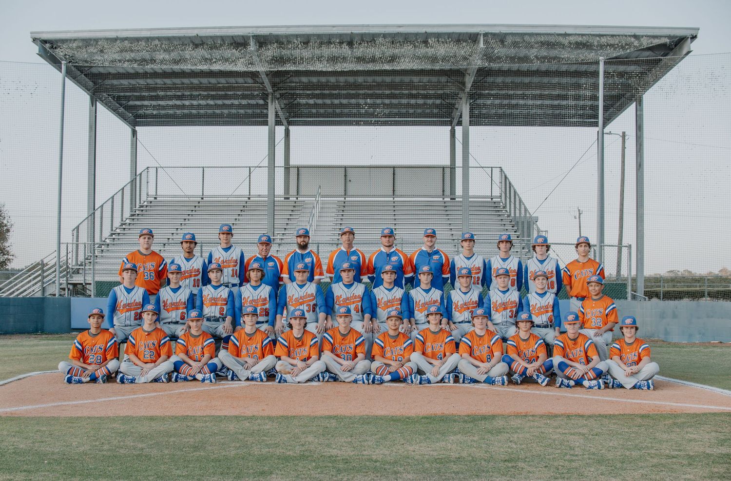 Large group team photo of baseball players in blue and orange uniforms on a sports field.