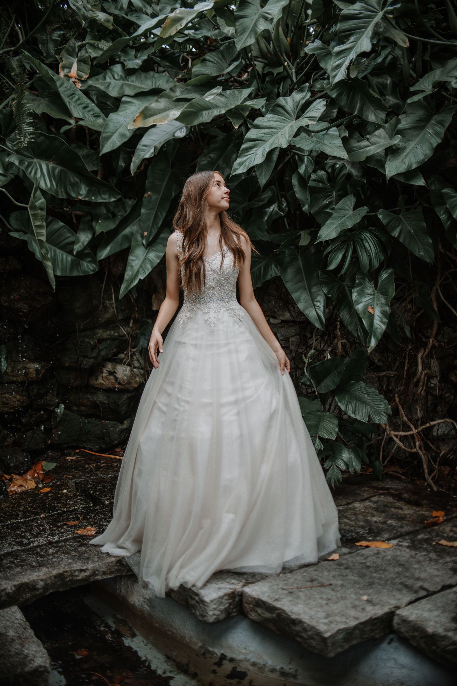 Romantic bridal portrait with flowing white gown against lush tropical foliage.