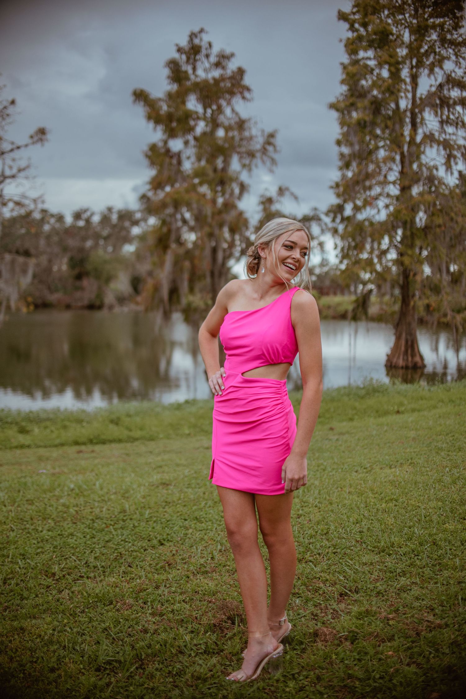 Person in bright pink athletic wear poses on grassy hill near water.