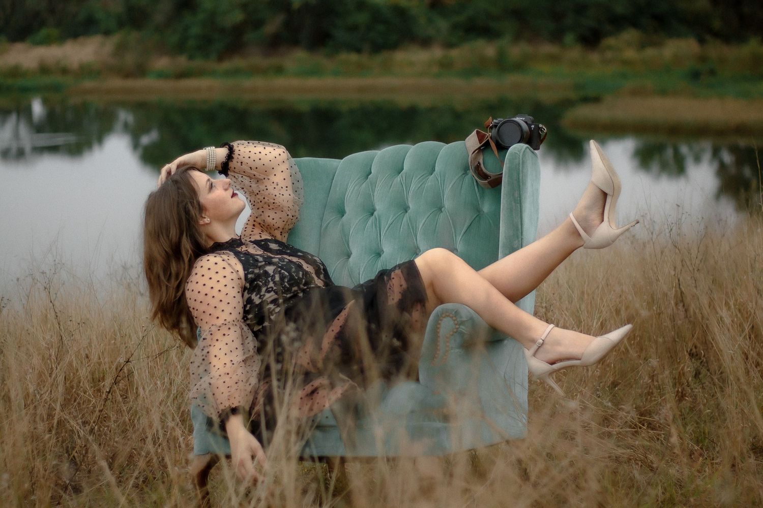 A teal velvet sofa placed outdoors in tall grass against a scenic backdrop.