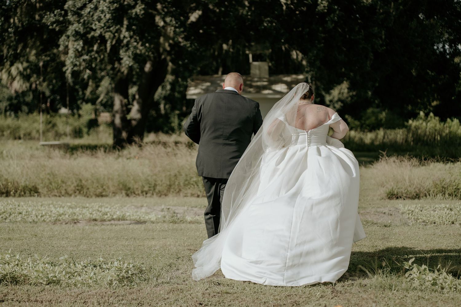 Newlywed couple sitting together in a grassy field with the bride wearing a flowing white wedding dress.
