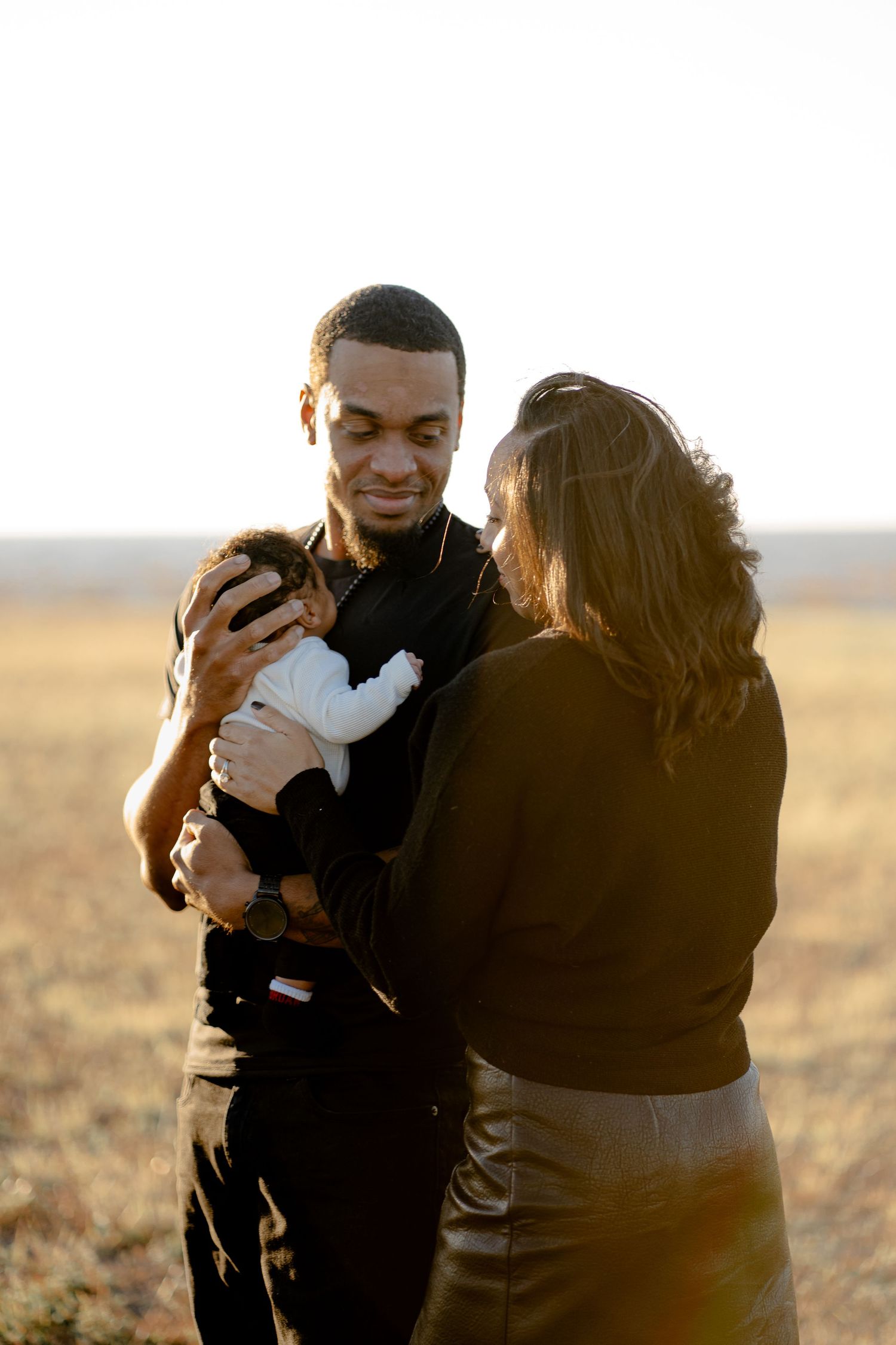 Parents share emotional moments with their newborn baby during a sunset photoshoot.