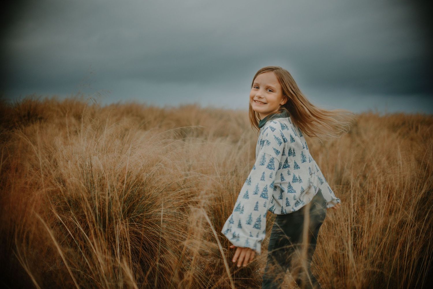 Young person twirling in a field of tall grass during golden hour.