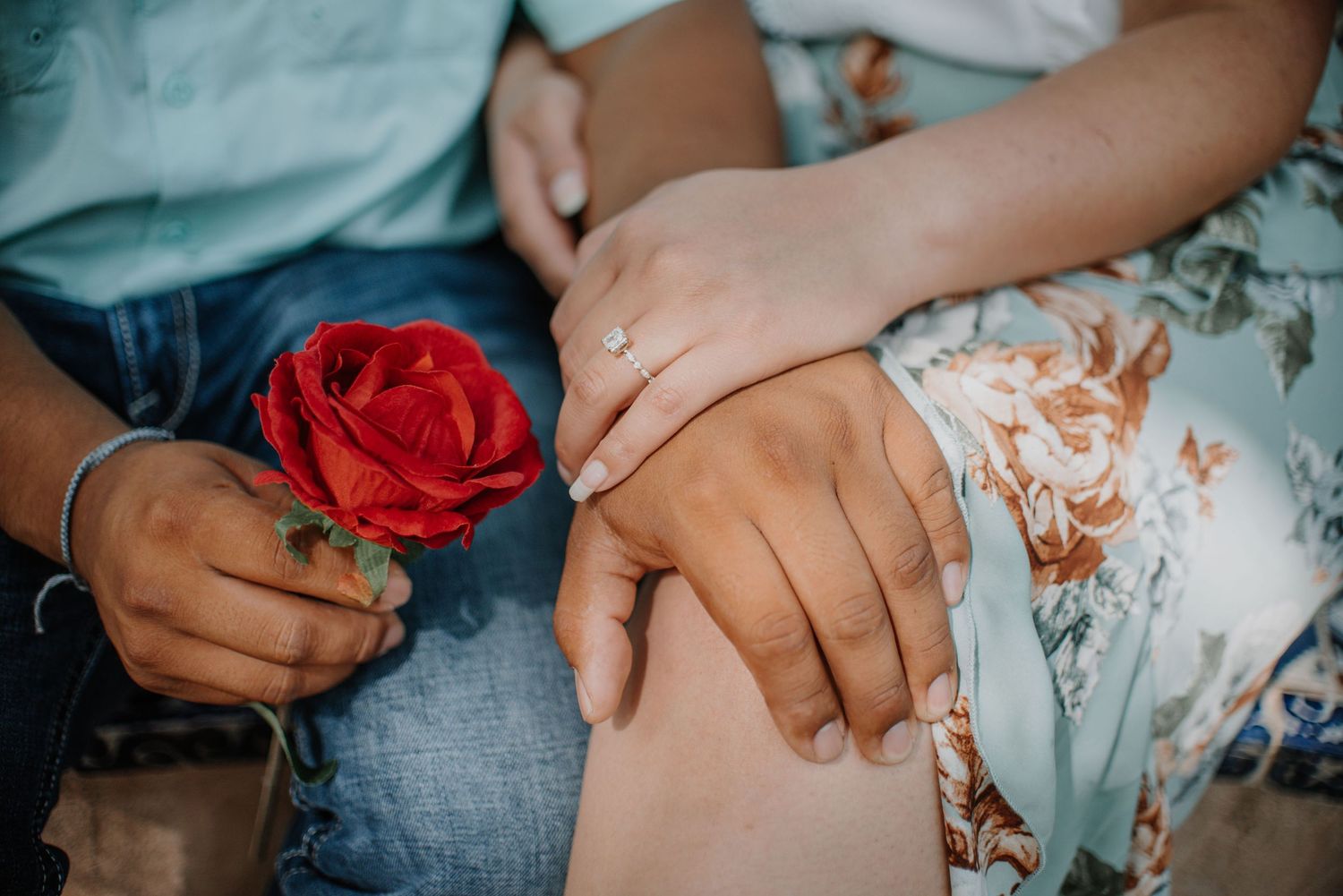 Close-up of hands holding a red rose against floral dress and denim.