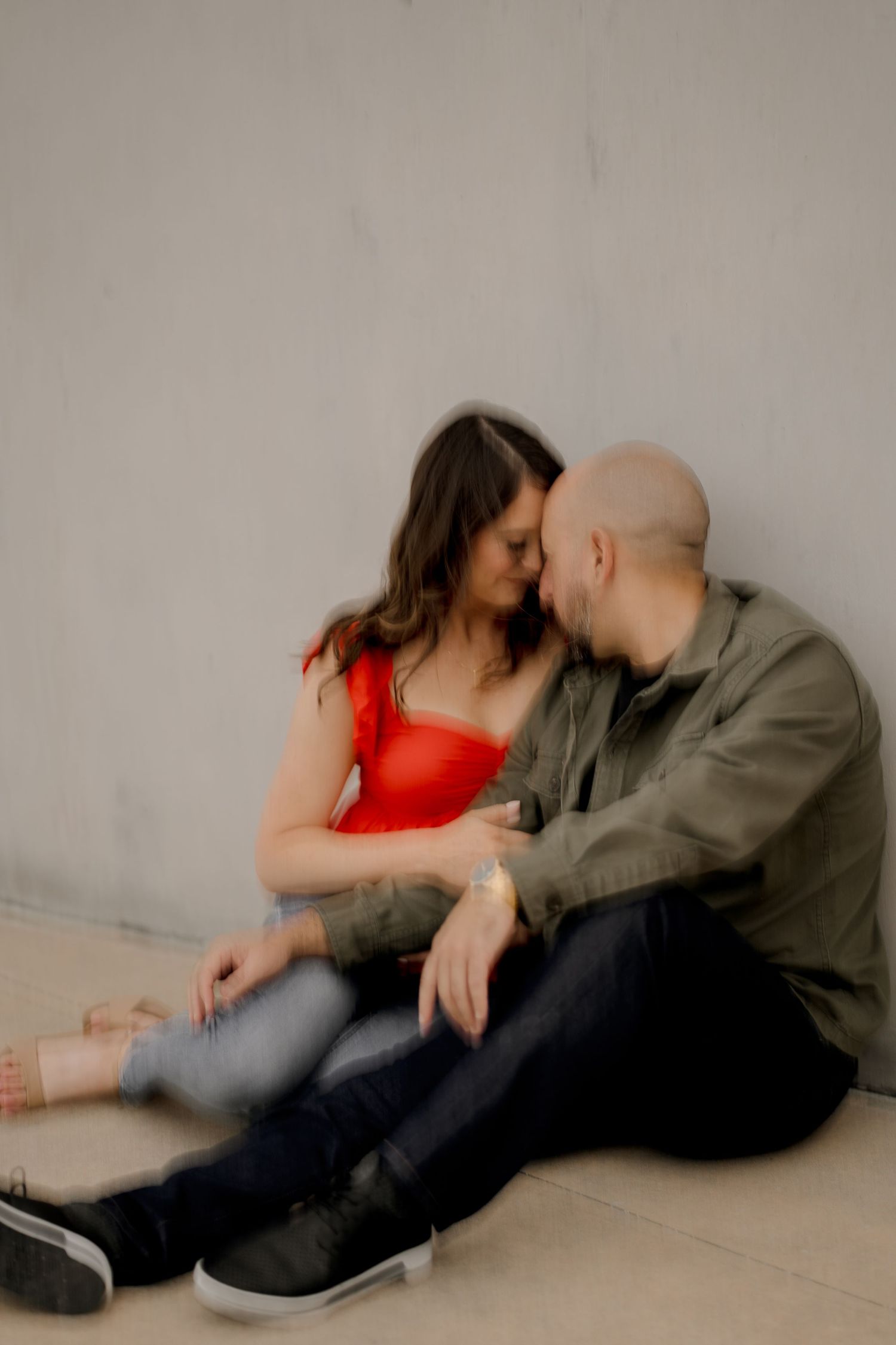 Intimate couple sitting together against plain wall in casual attire.