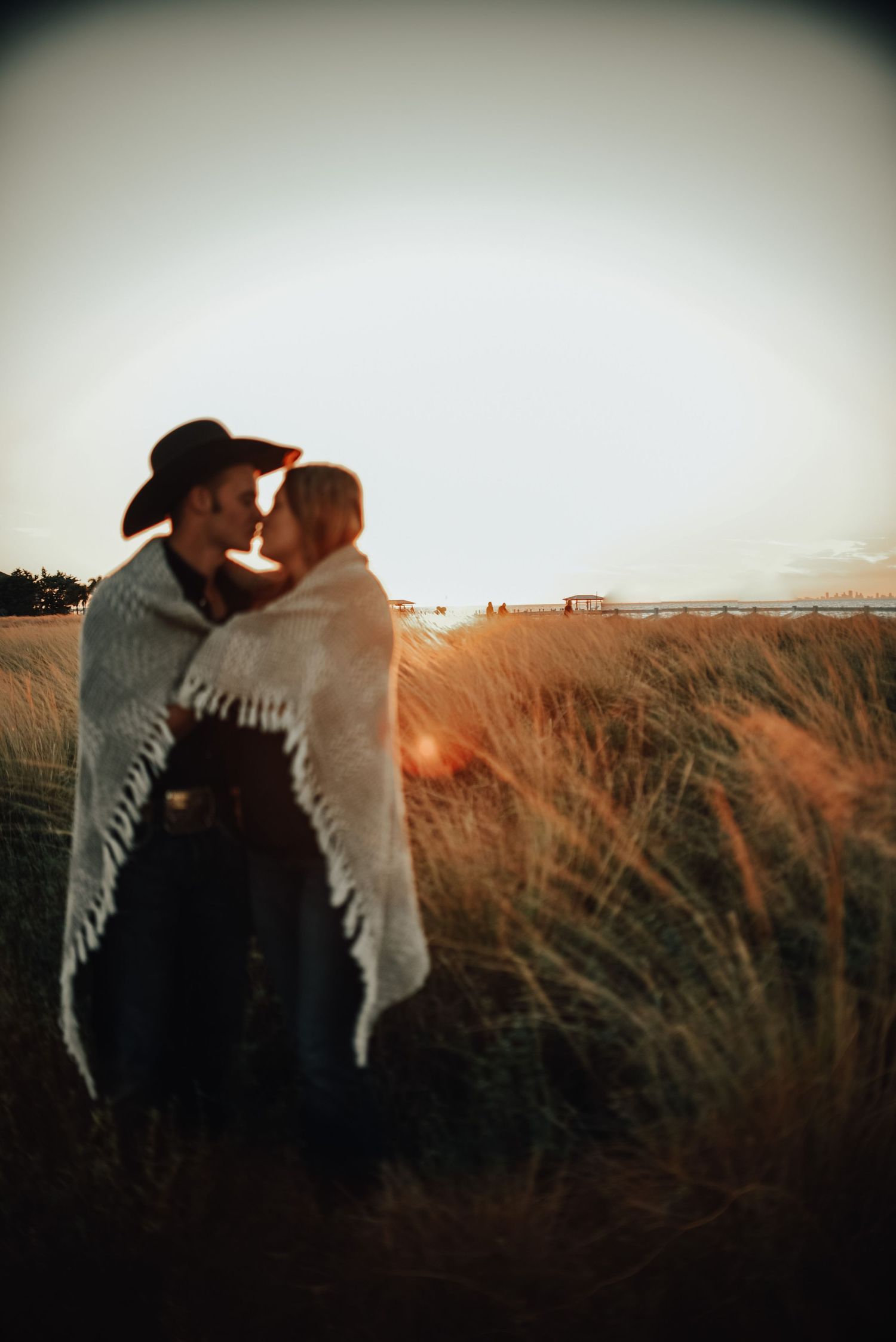 Romantic silhouette of a couple embracing in a golden field at sunset with a cowboy hat visible.