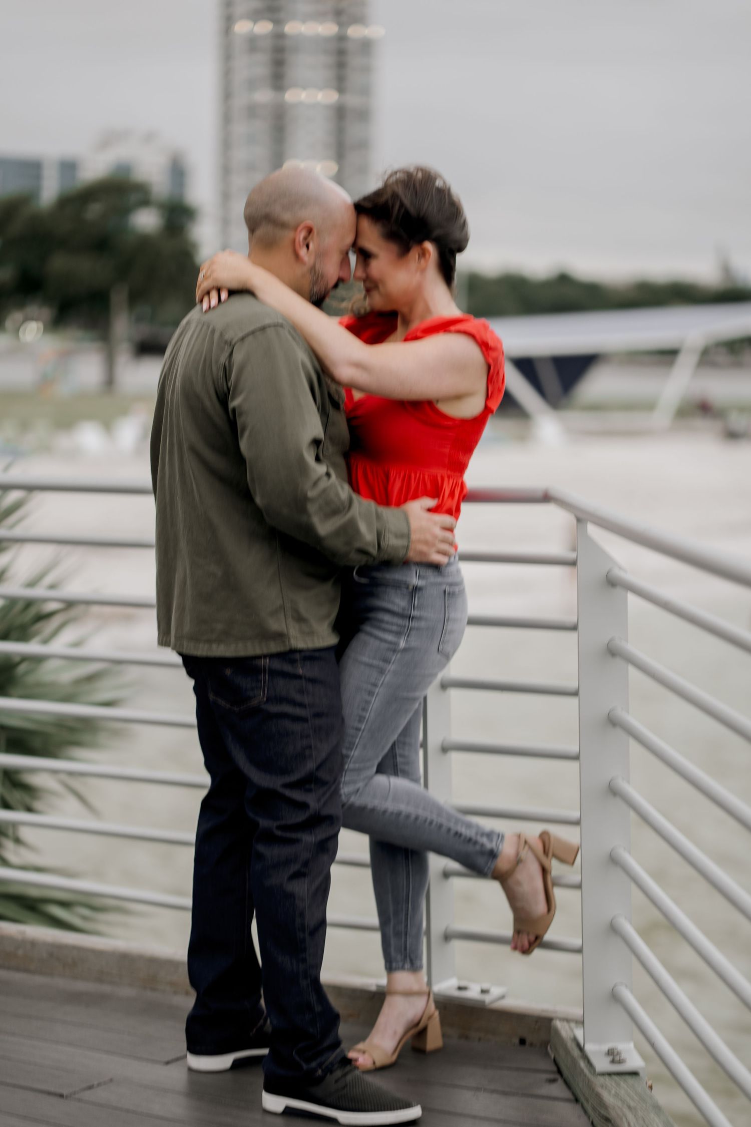 A couple shares an intimate moment against white railings overlooking water.