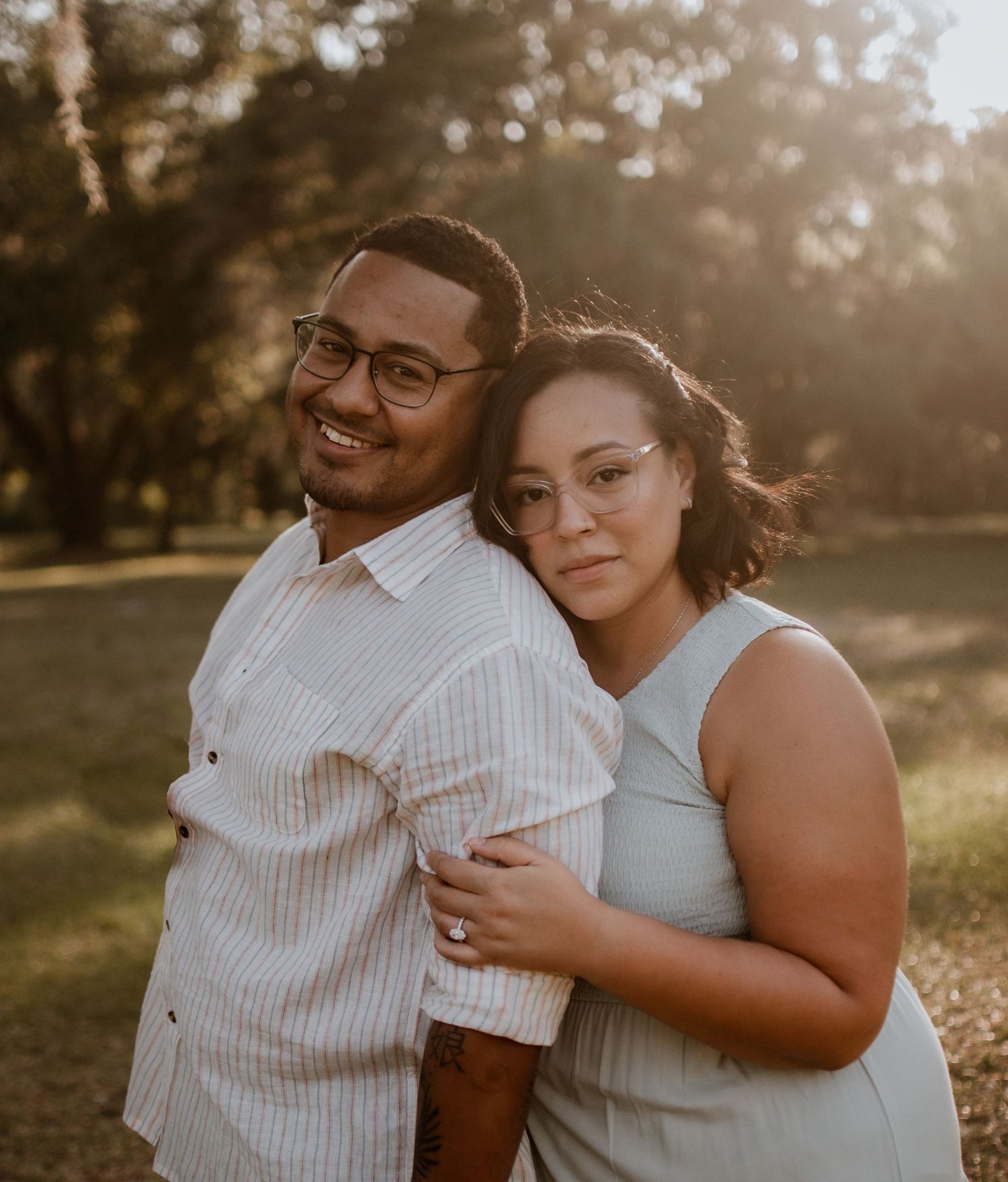 A couple embraces in golden sunlight during an outdoor photoshoot.