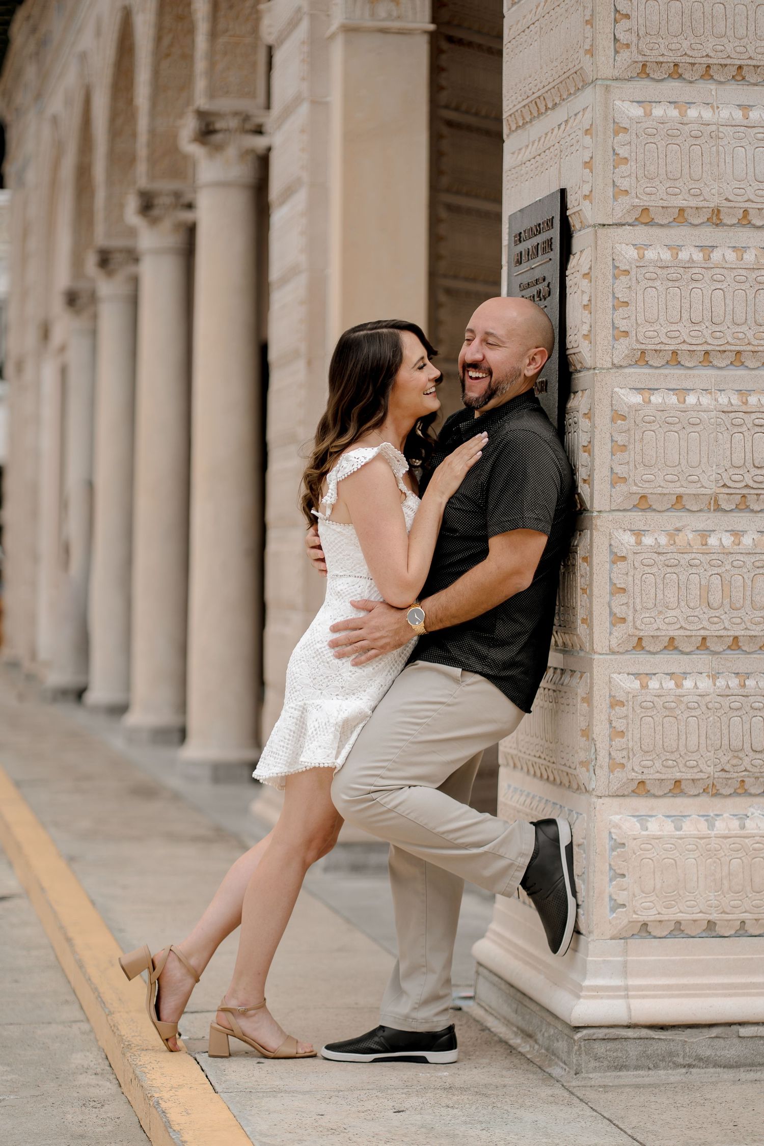 Romantic couple embracing against ornate architectural column.