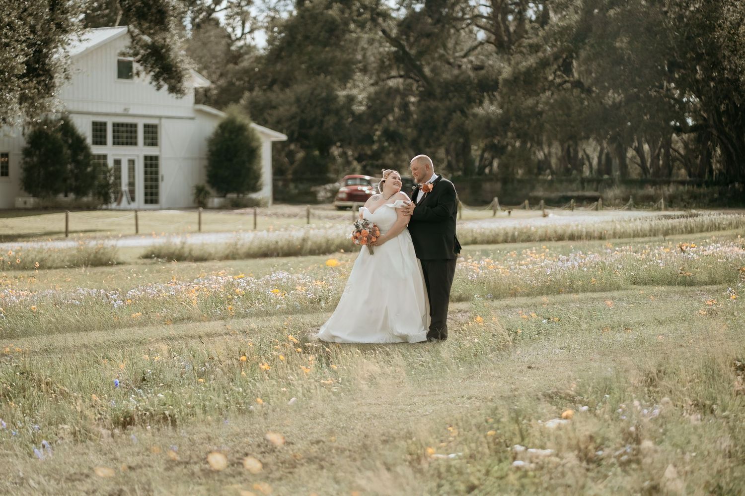 Wedding couple walking through a scenic countryside field during golden hour.