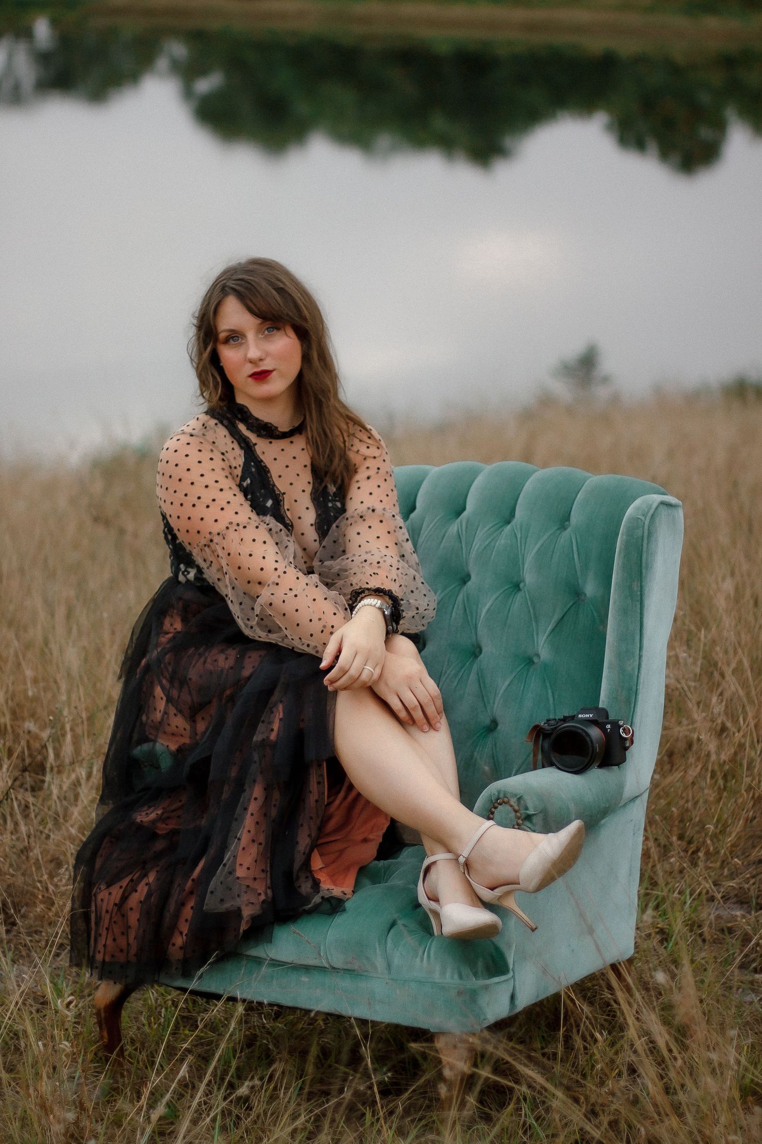 Fashion portrait on teal tufted chaise featuring polka dot blouse and vintage styling.