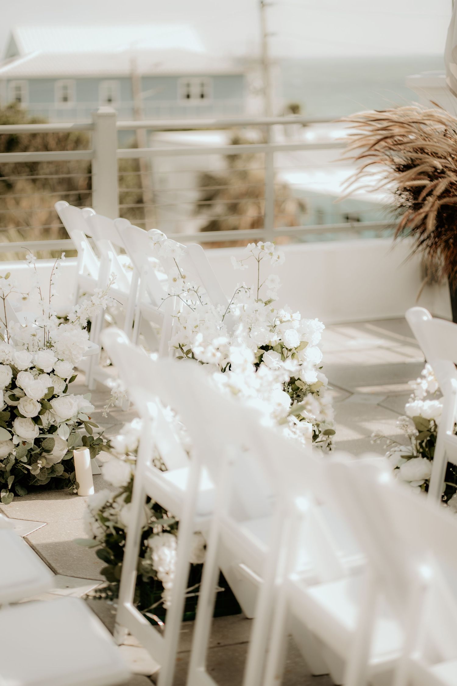 White chairs and floral decorations line an elegant outdoor wedding ceremony setup with ocean views.