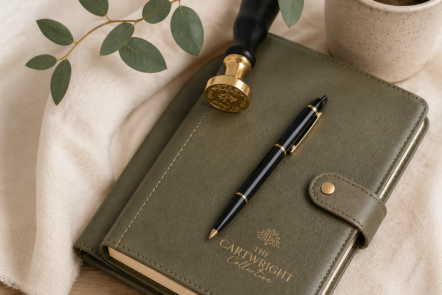 Elegant olive green leather journal with gold wax seal stamp and black fountain pen on soft linen background.