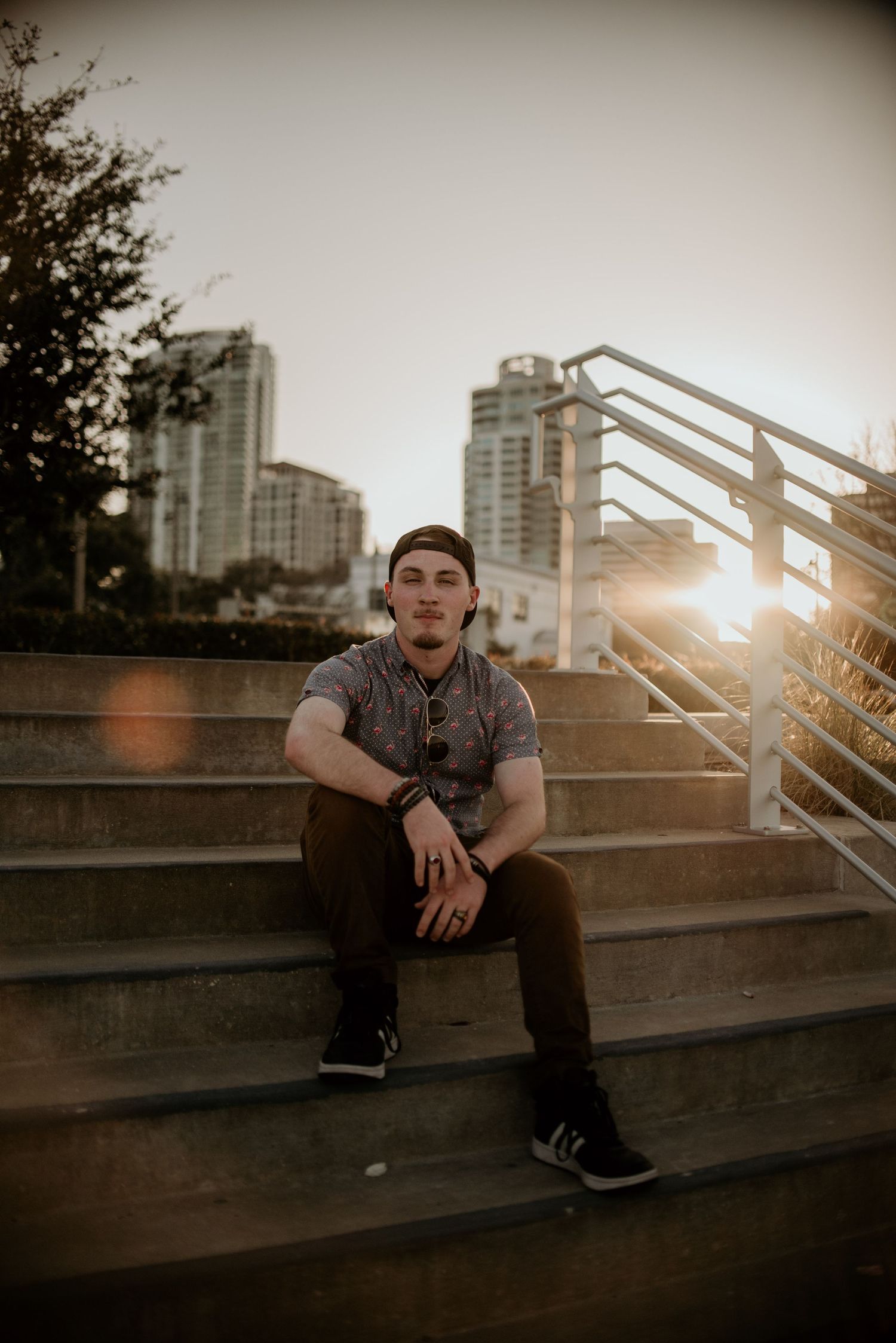 Person sitting on concrete steps at sunset with city buildings in background.