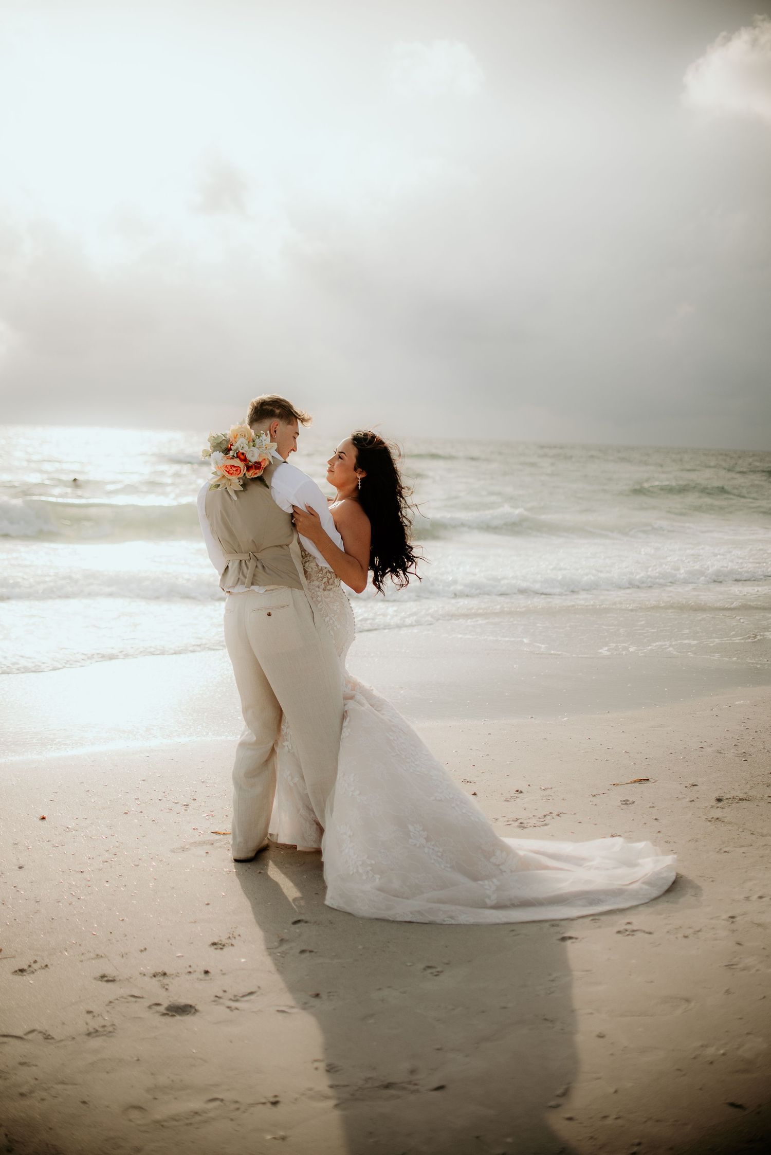 A romantic couple embraces on a misty beach during their wedding photoshoot.
