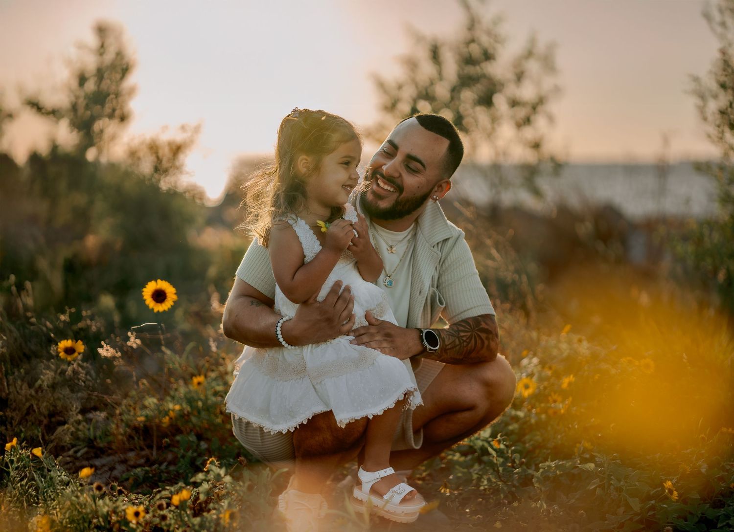 Father and daughter share joyful moment among sunflowers at sunset.