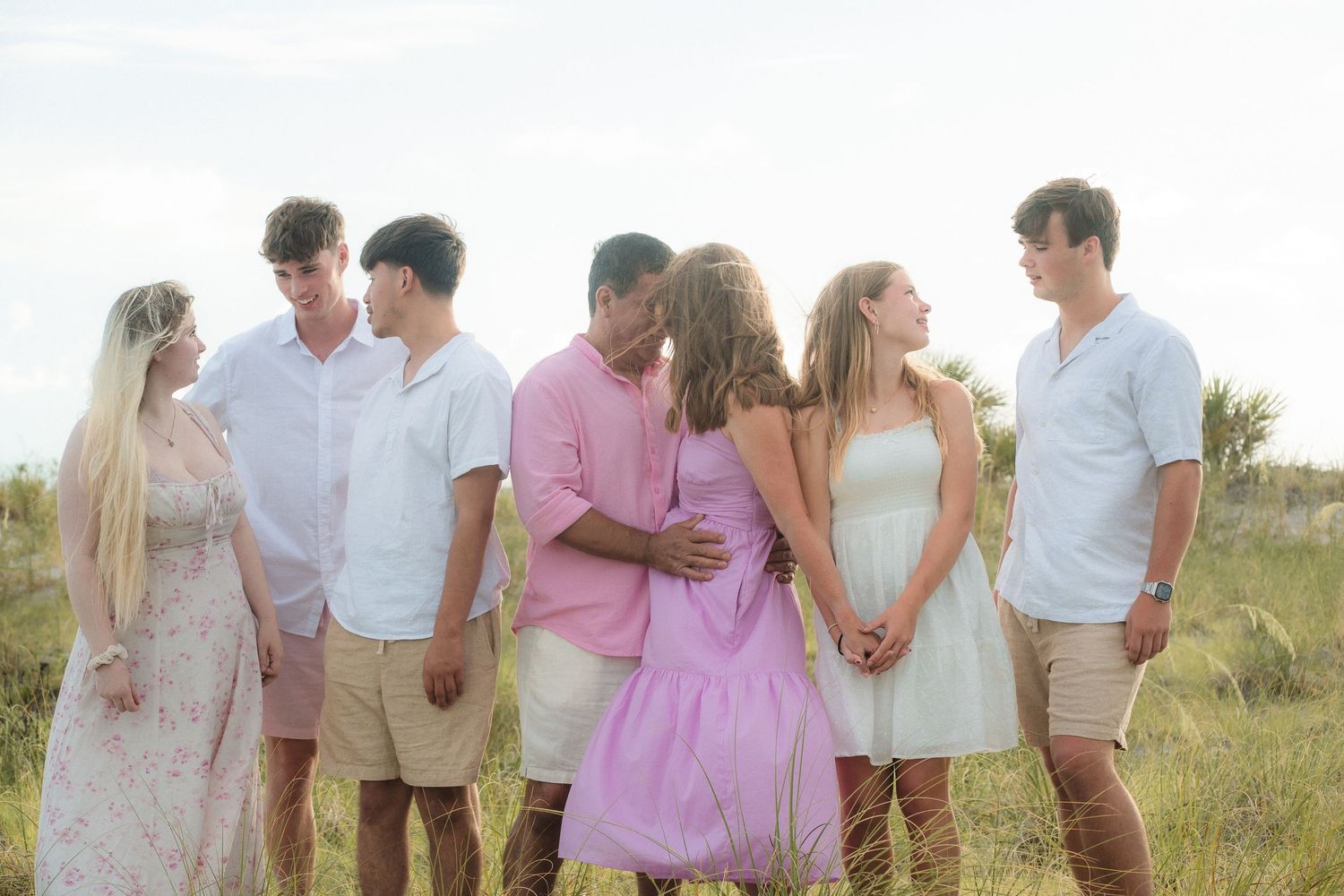 Group portrait in soft pastel outfits during golden hour in grassy field.
