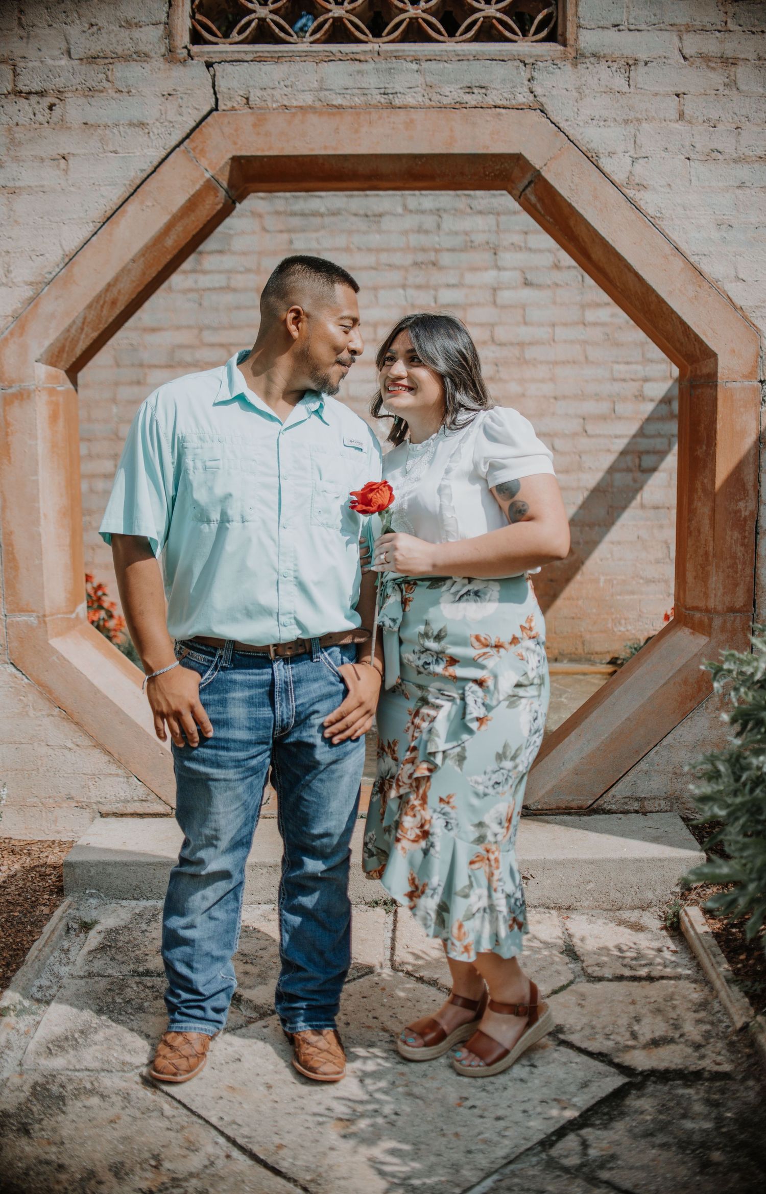 Couple sharing a tender moment against a geometric brick archway with a red rose.