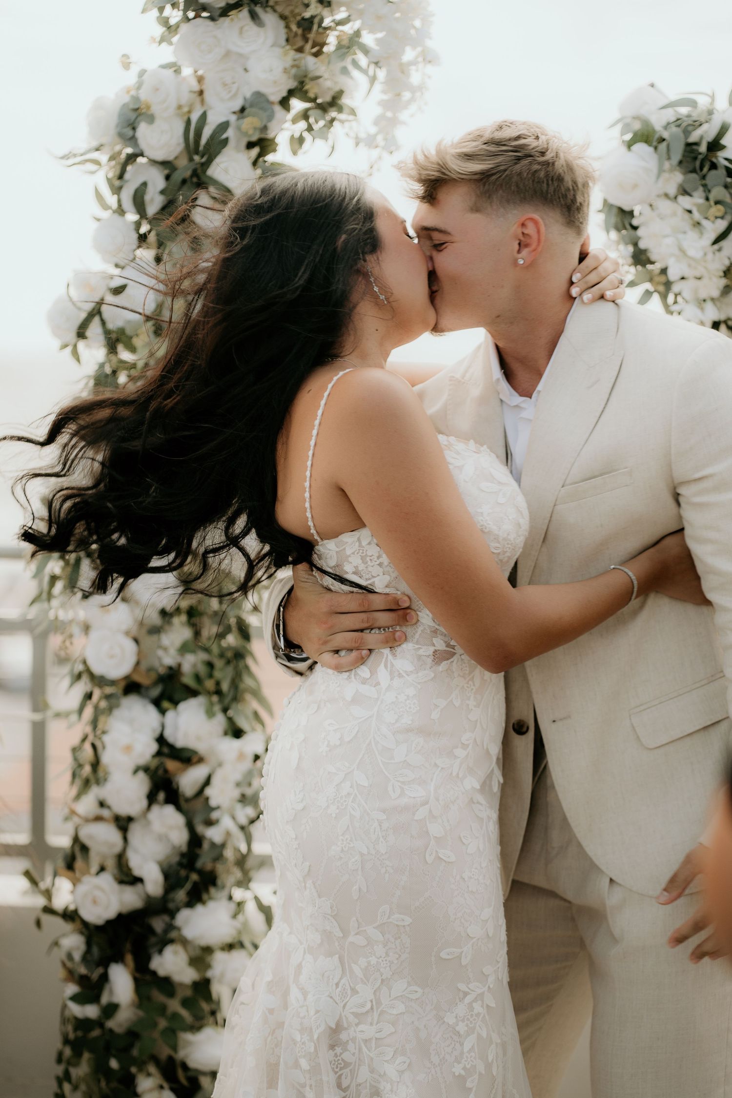 Newlyweds sharing romantic kisses under a floral arch during their wedding ceremony.