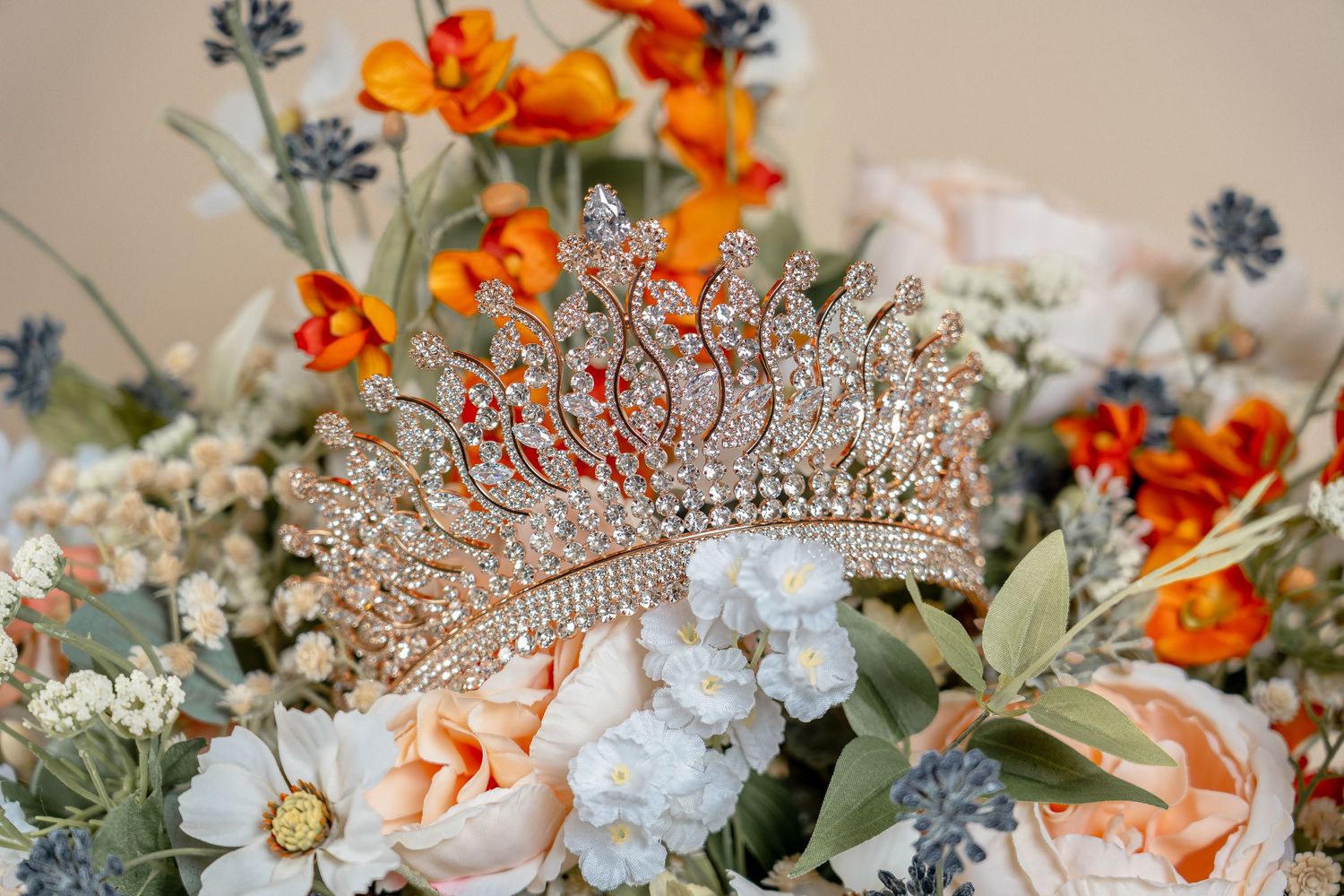 Close-up of orange and white floral arrangements with a sparkling tiara.