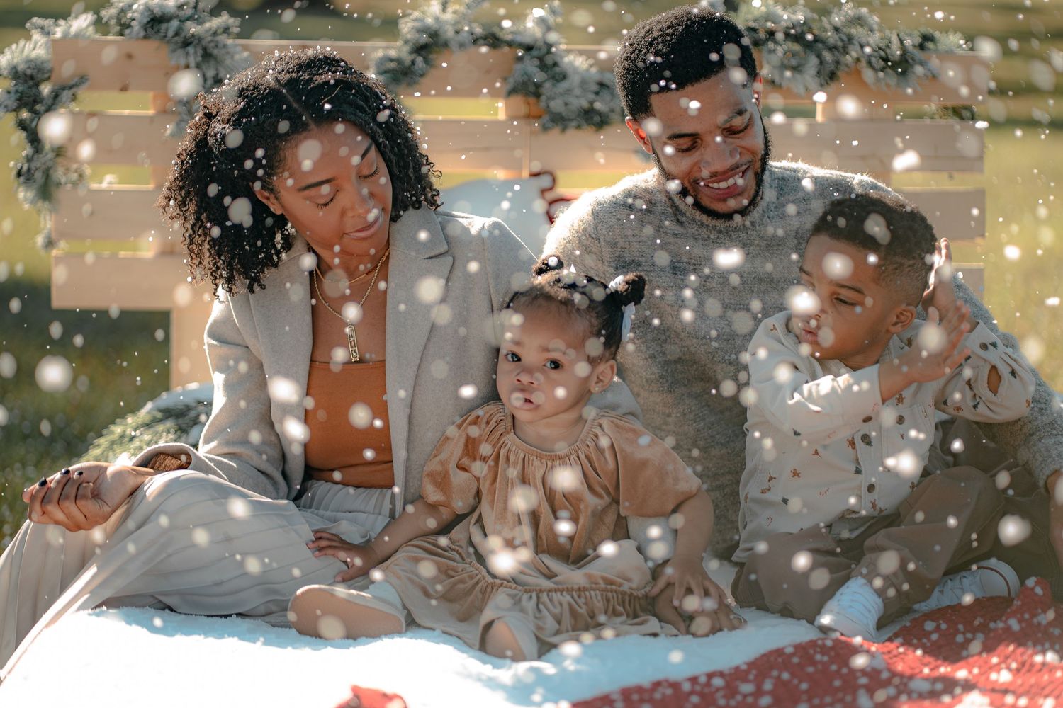 family christmas photoshoot with snow on a rustic bed in a grassy field and christmas decorations.