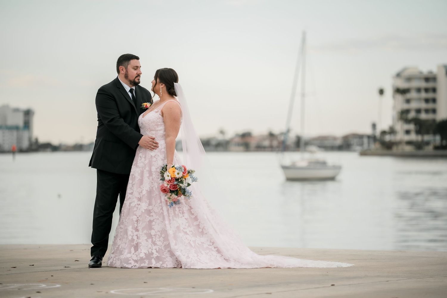 Waterfront wedding portrait with couple against marina backdrop at sunset.