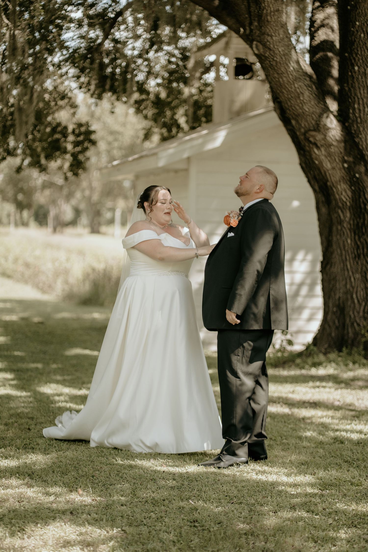A sweet wedding moment shared between a couple under a large tree.