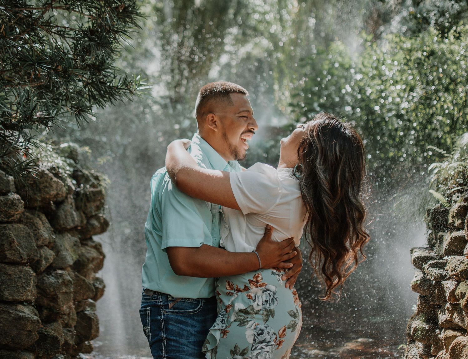 Joyful couple laughing and embracing in a misty garden setting with stone walls.