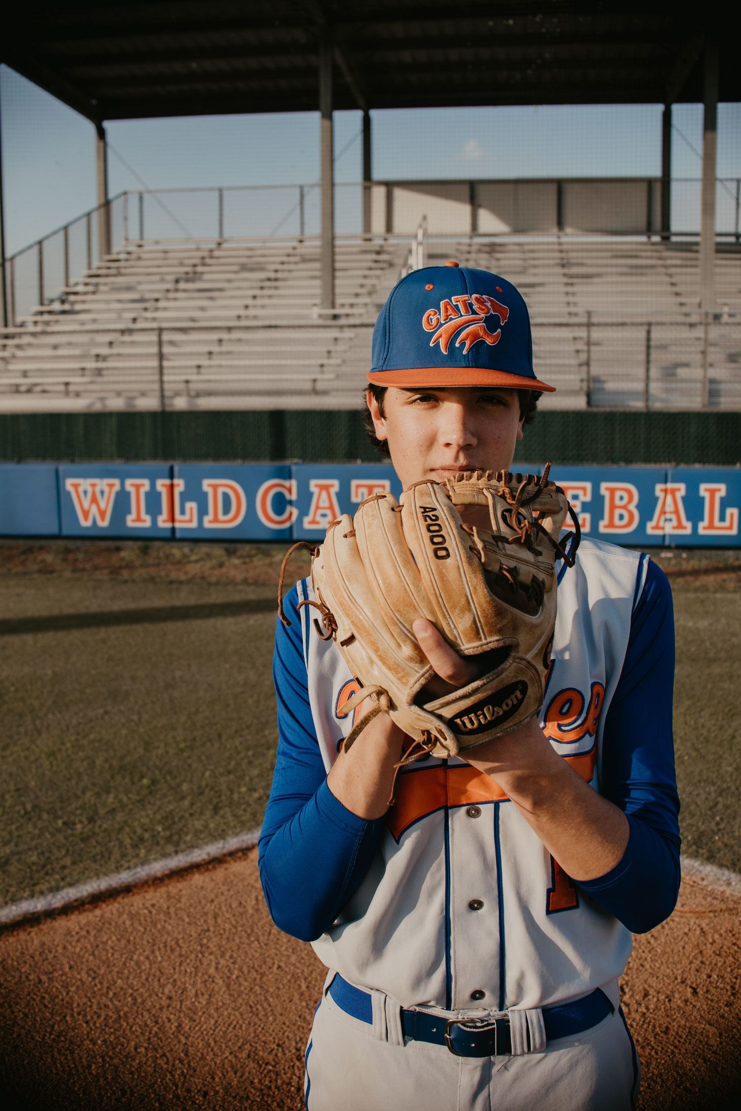 Baseball player in blue uniform holding glove in front of face on baseball field.